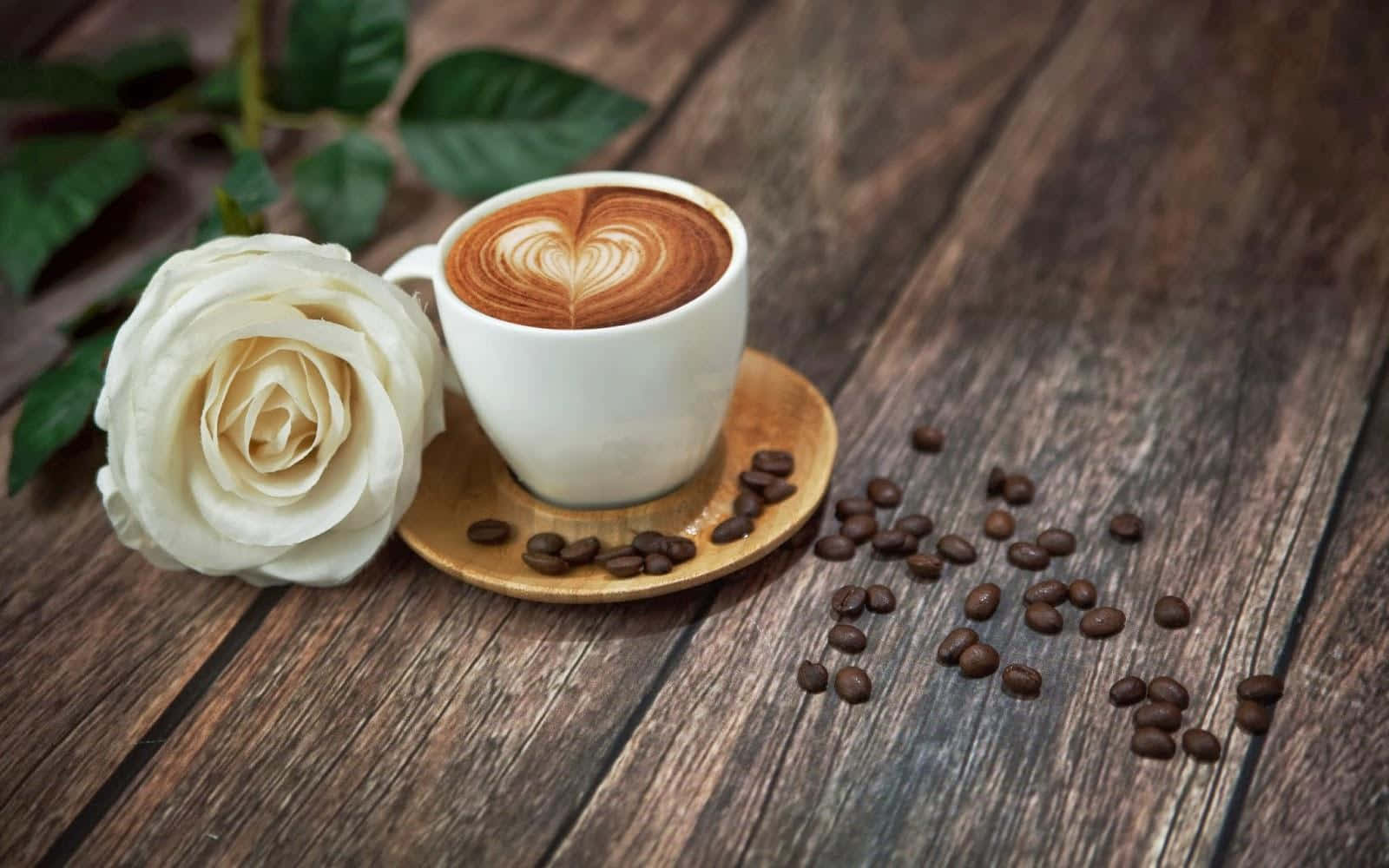 Coffee Aesthetic 桌布 壁紙 — 一朵白玫瑰和一杯拉花咖啡放在一張散落著咖啡豆的質樸木桌上。