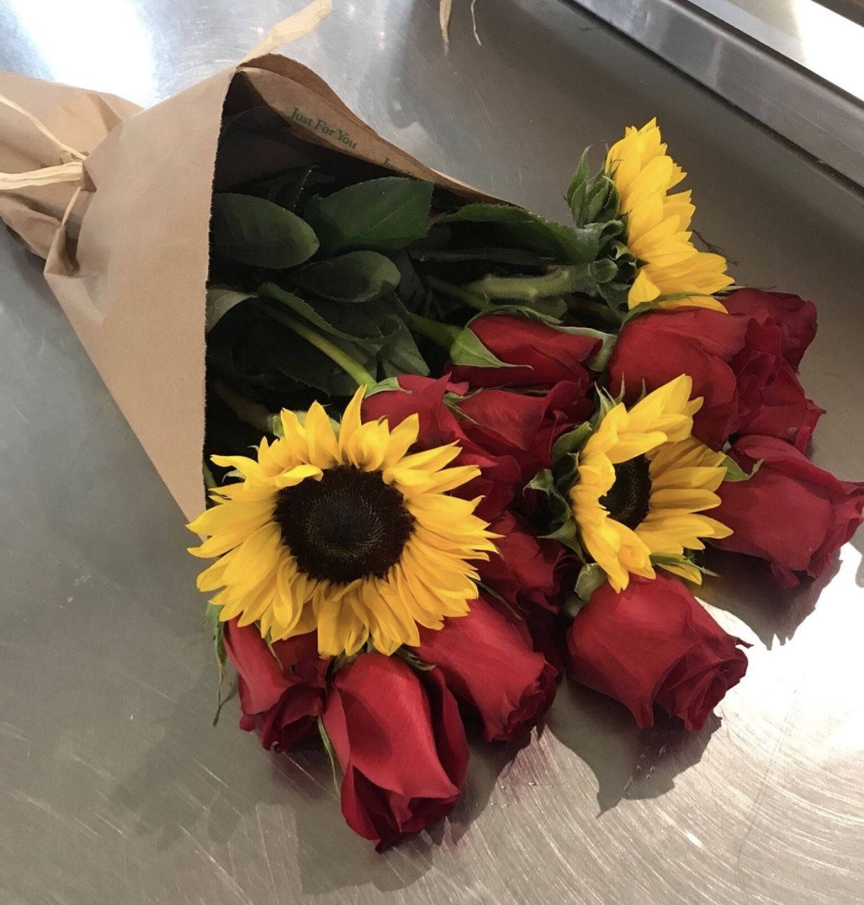 Red Roses 桌布 壁紙 — 一束充滿活力的向日葵和深紅玫瑰，用棕色紙包裹，放在拉絲金屬表面上。