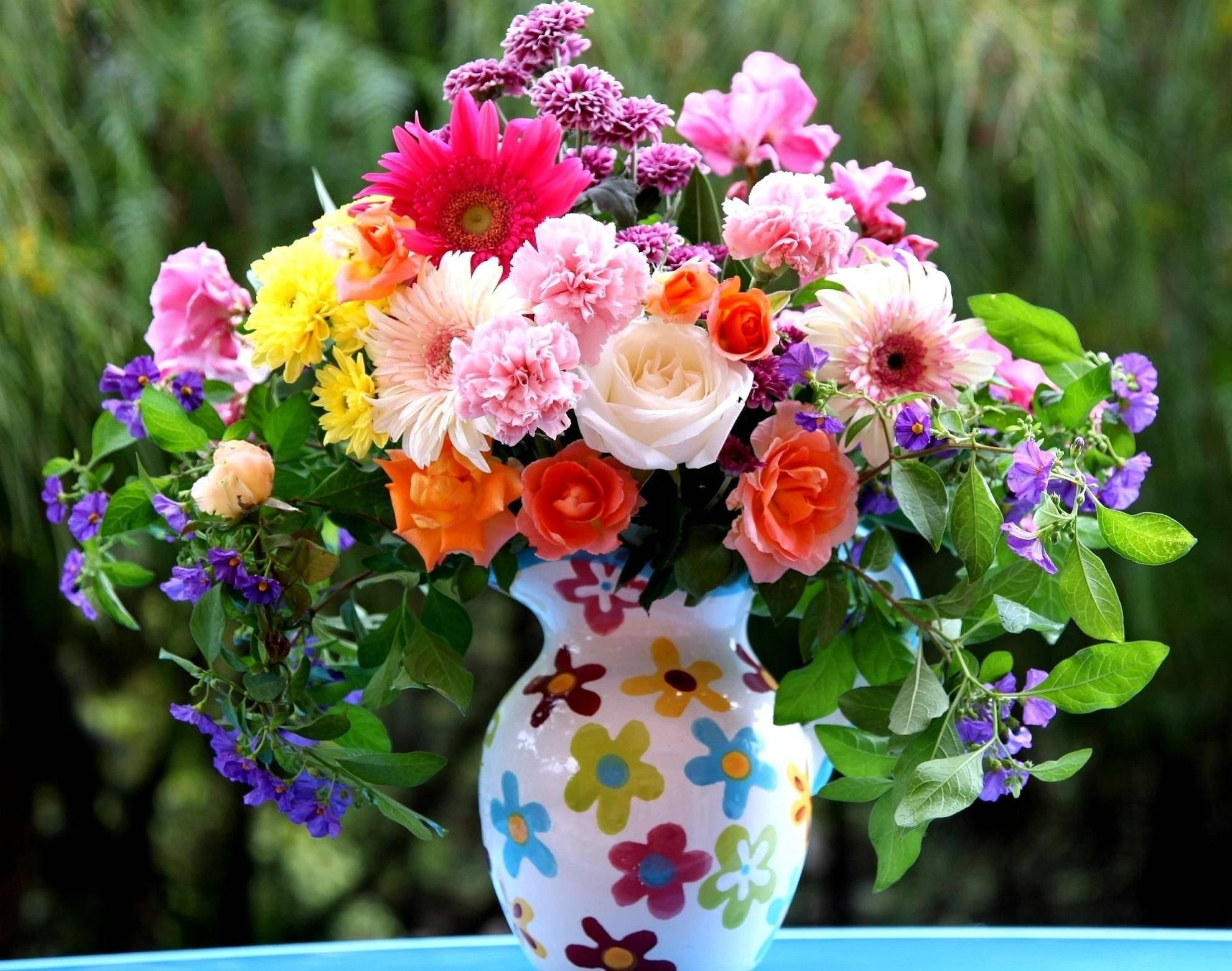 花 桌布 壁紙 — 一束充滿活力的粉紅色、橙色、黃色和紫色花朵從一個裝飾著彩色花朵的白色花瓶裡溢出，背景是模糊的綠色。
