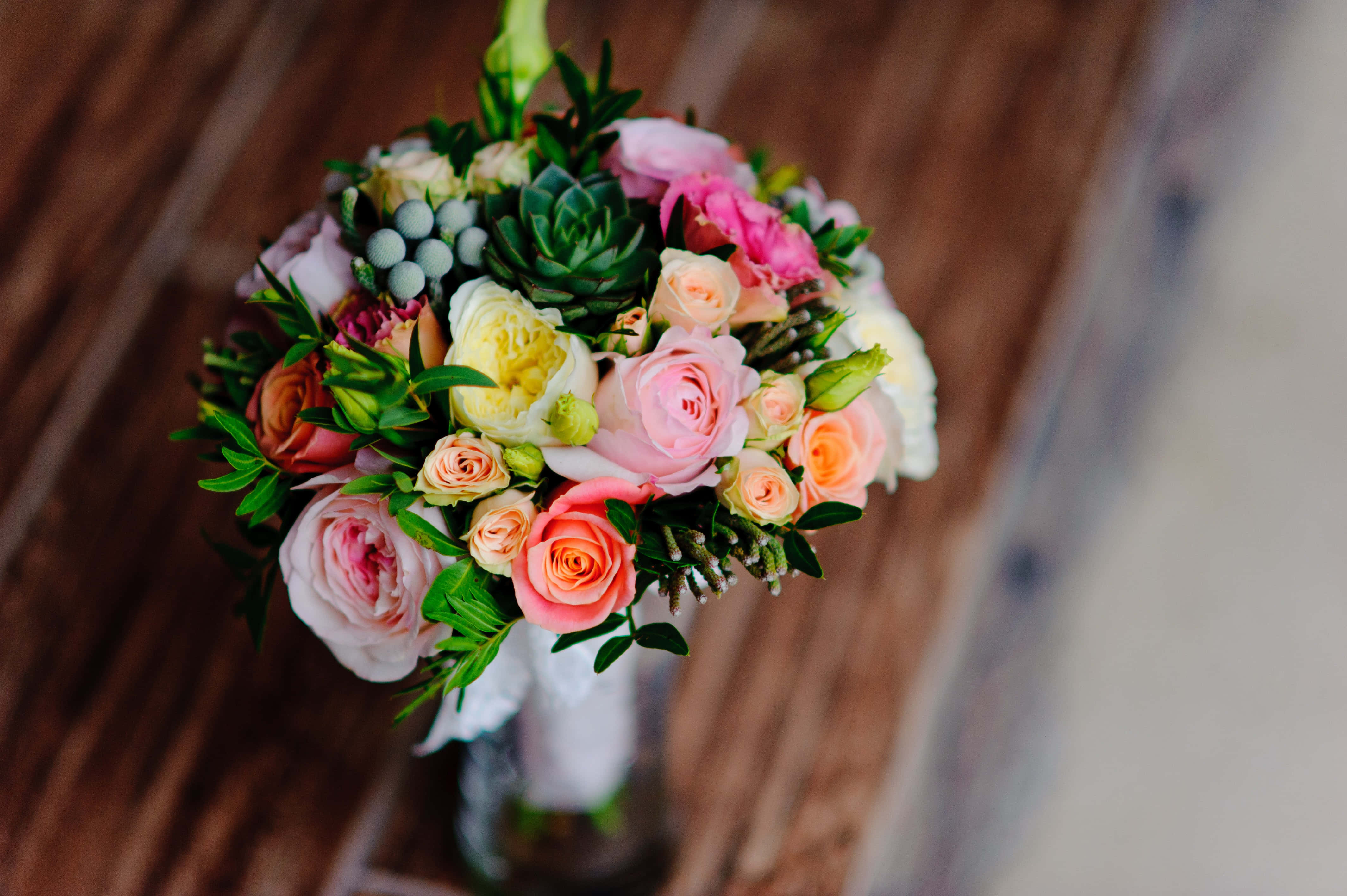 Bouquet 桌布 壁紙 — 一束充滿活力的粉紅蜜桃色和黃色玫瑰、多肉植物和漿果，放在一個玻璃花瓶裡，置於質樸的木桌上。