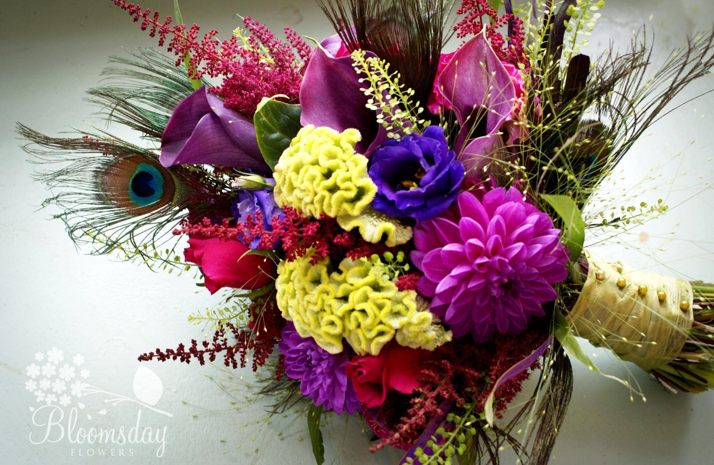 孔雀動圖 桌布 壁紙 — 一束充滿活力的紫色、粉紅色和黃色花朵，配以孔雀羽毛和綠色植物，背景為白色。