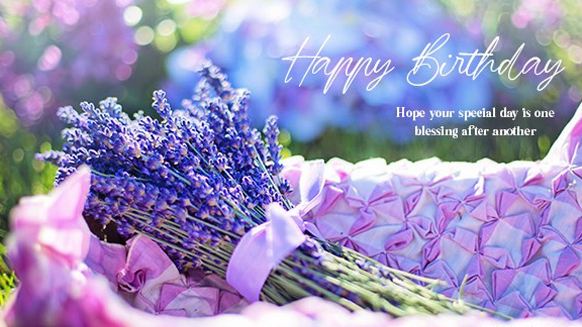 Happy Birthday Flower 桌布 壁紙 — 一束充滿活力的紫色薰衣草，用絲帶紮著，放在有紋理的粉紅色紙上，背景是陽光下的散景效果，並帶有生日文字。