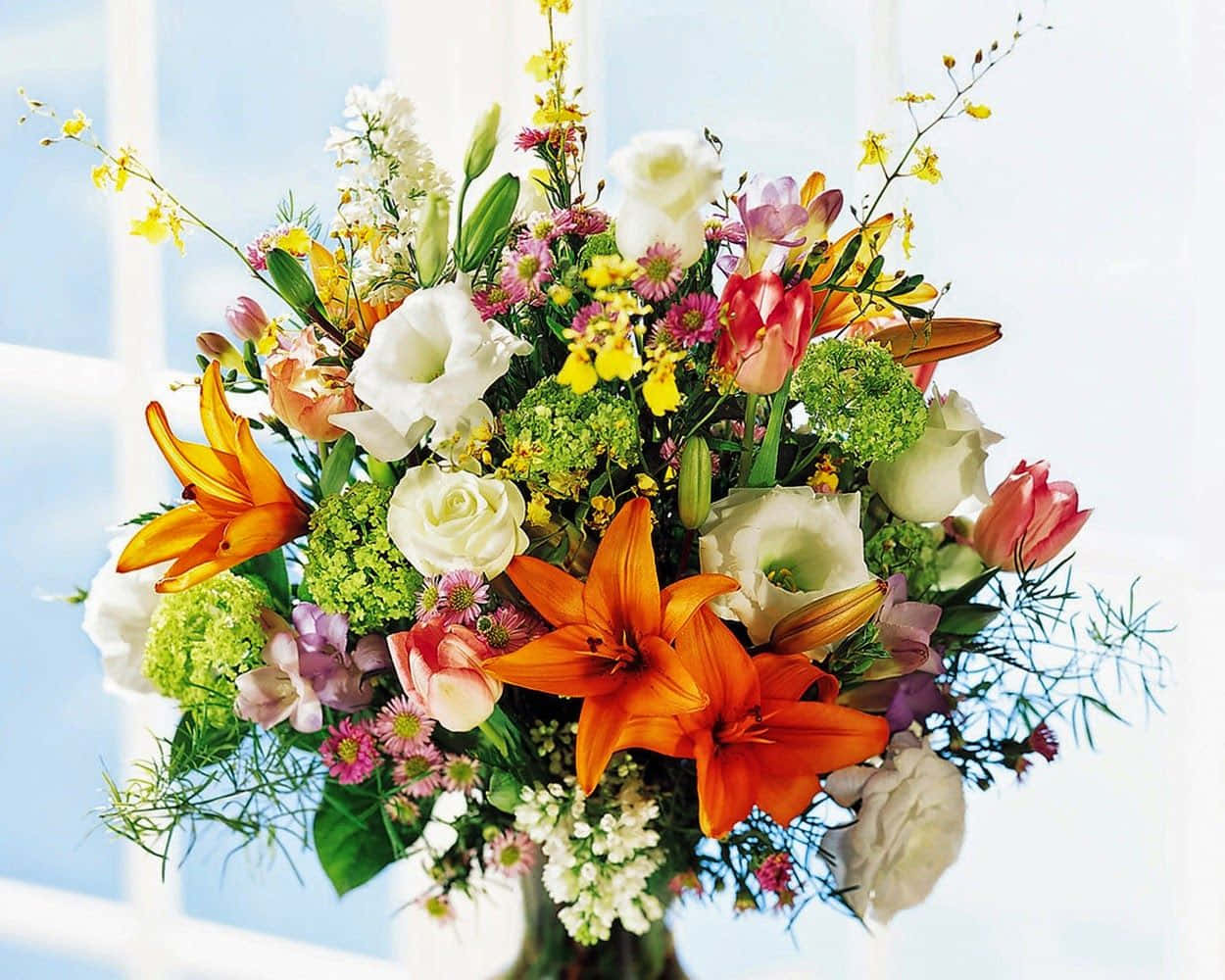 Flower Arrangement 桌布 壁紙 — 一束充滿活力的花束，包含橙色百合、白玫瑰和各種色彩繽紛的花朵，擺放在明亮窗戶前的花瓶中。