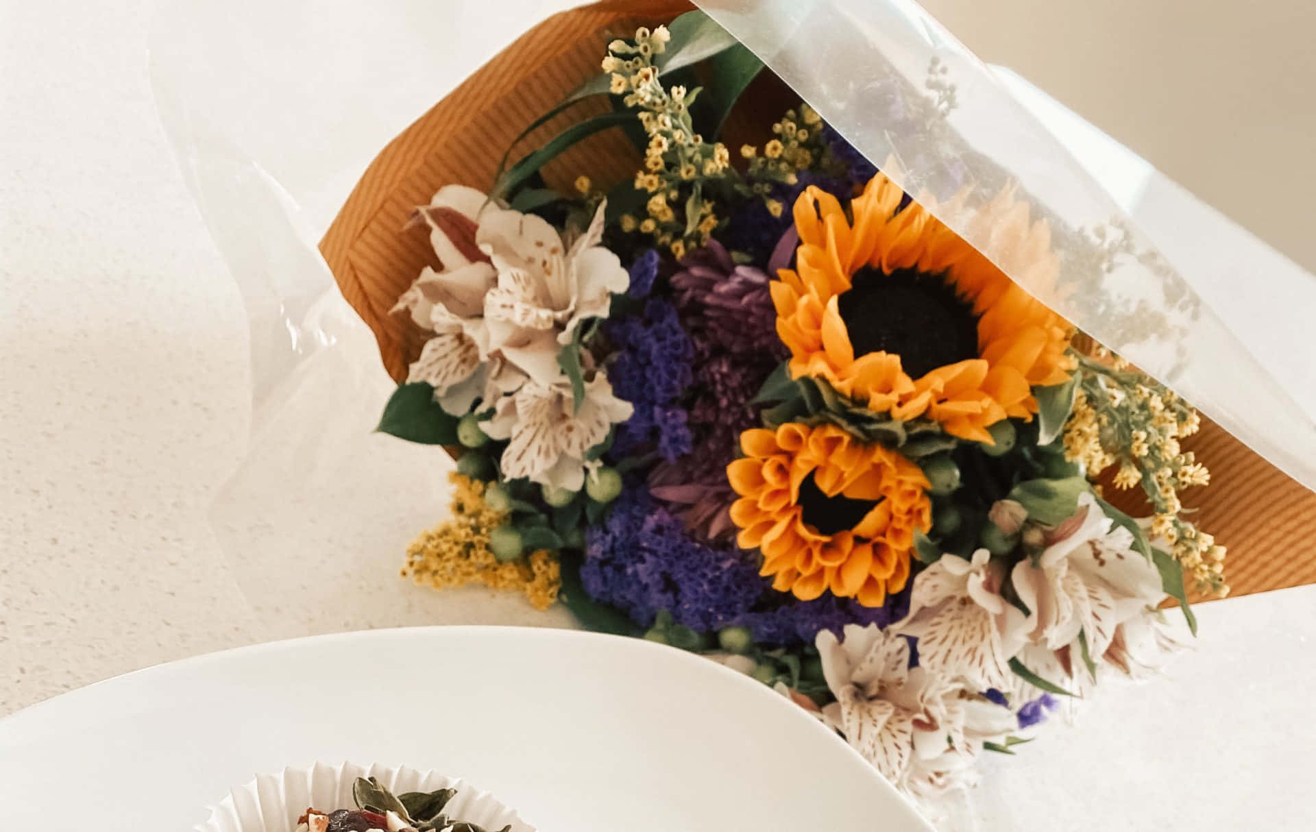 花 桌布 壁紙 — 一束充滿活力的花束，包括向日葵、紫色繡球花和奶油色六出花，用棕色紙和透明玻璃紙包裹，放在一個白色碗旁邊。