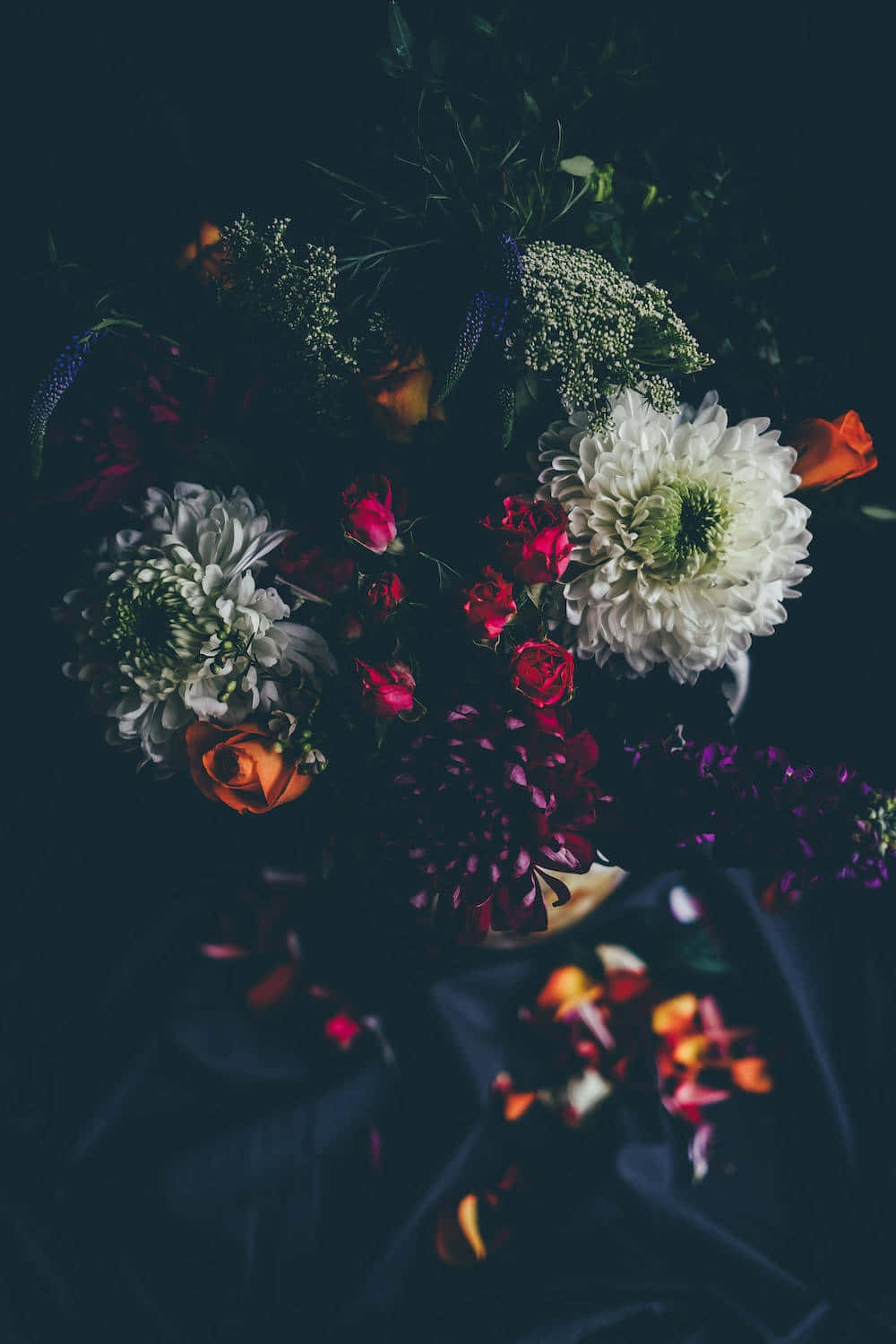 Dark Flower Aesthetic 桌布 壁紙 — 一束戲劇性的白色、紅色和橙色花朵，搭配綠色植物，置於陰暗憂鬱的背景前。