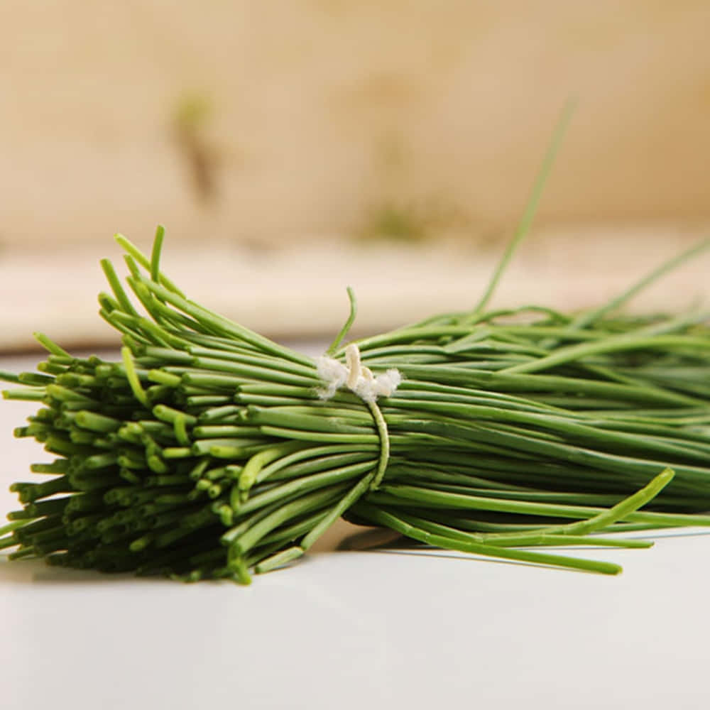Food Photography 桌布 壁紙 — 一束新鮮的翠綠韭菜用白色繩子綁著，放在潔白的表面上，背景是柔和的米色。