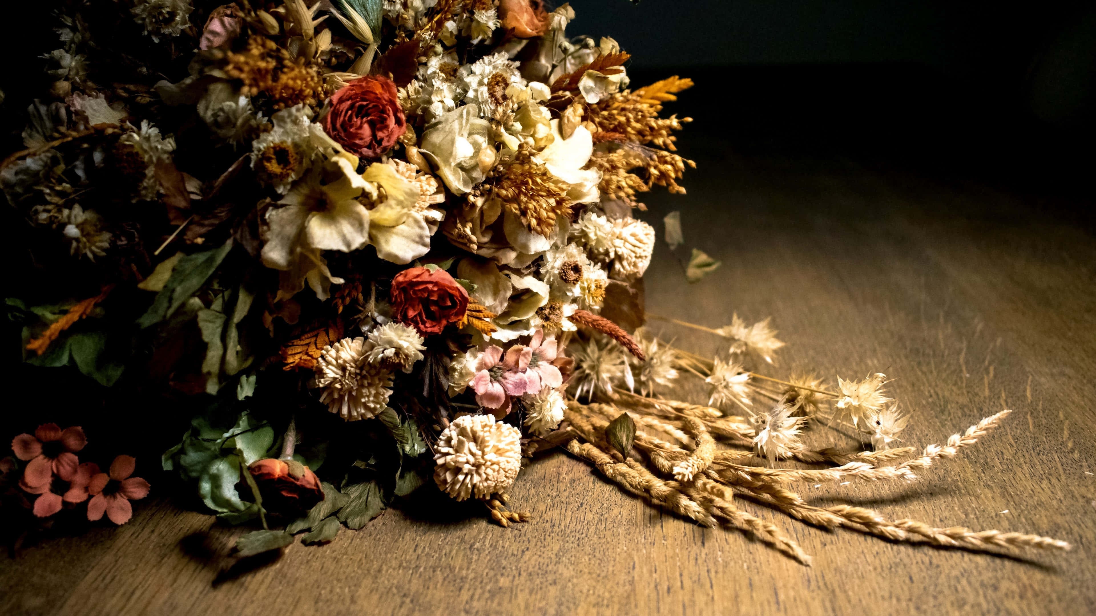 Dried Flowers 桌布 壁紙 — 一束樸實的乾花和小麥在柔和的方向性燈光下散落在溫暖的木質表面上。