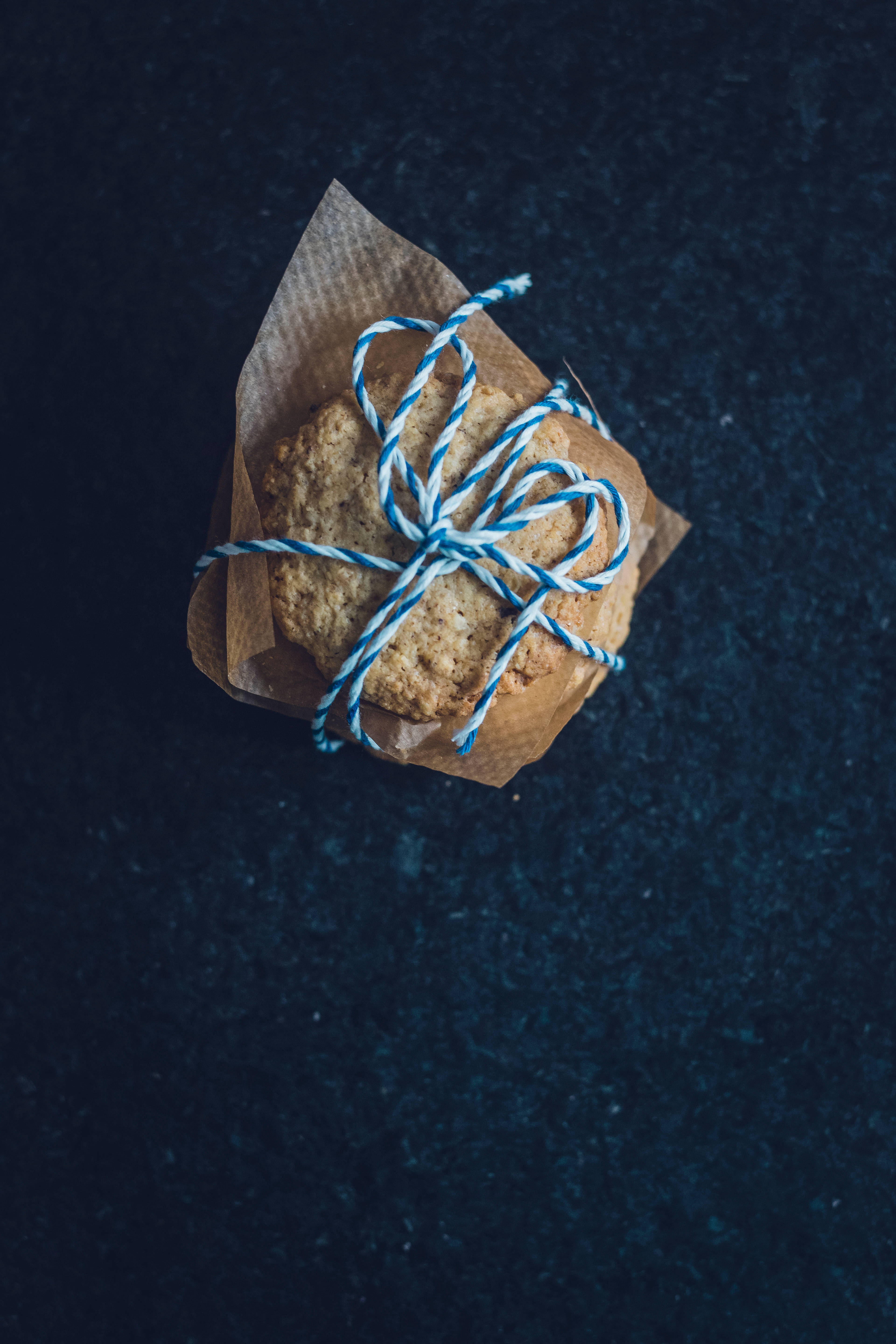 Pastries 桌布 壁紙 — 一束用藍白麻繩捆紮的鄉村燕麥餅乾，放在棕色紙上，背景為深色紋理。