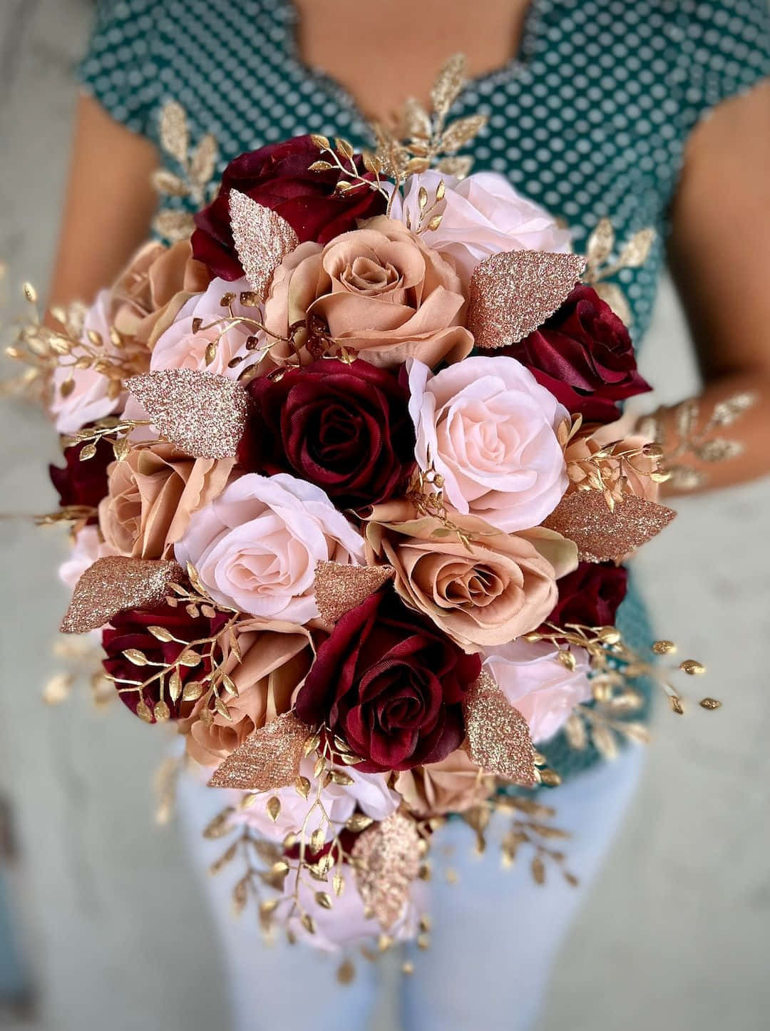 Roses Wedding 桌布 壁紙 — 一束由深紅和淡粉紅玫瑰組成的豐盛花束，點綴著閃閃發光的金色葉片和葉子，由一位穿著波點上衣的人手持。