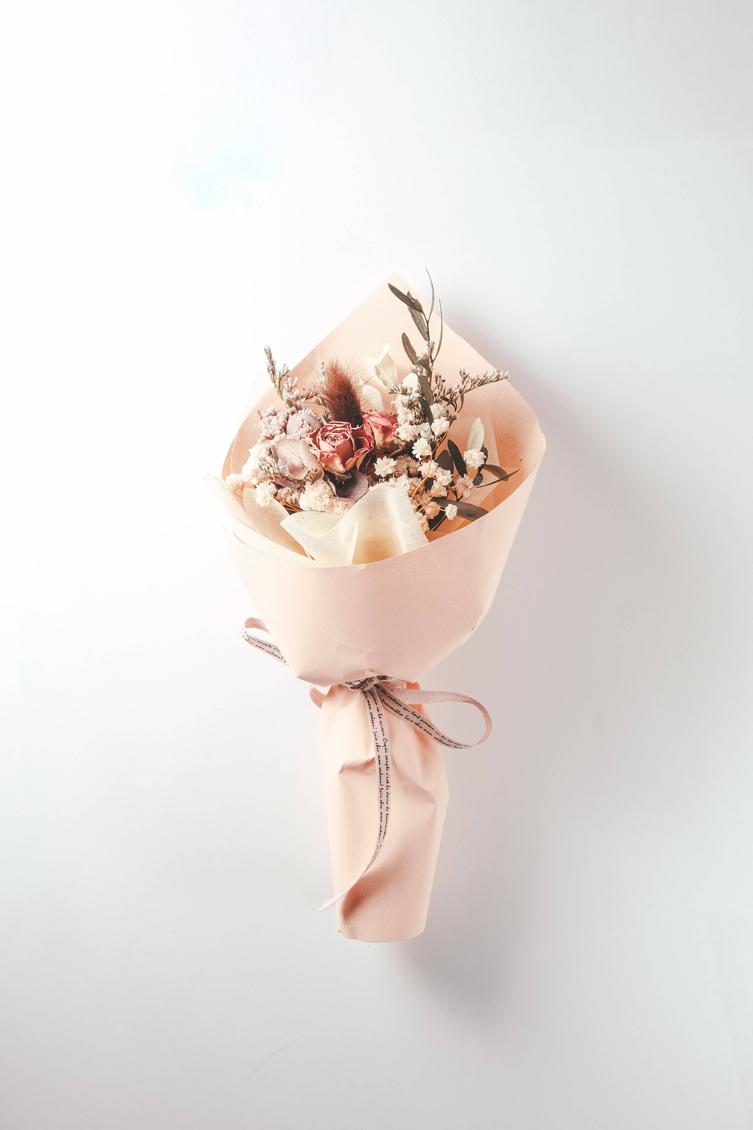 Roses 桌布 壁紙 — 一束精緻的乾燥花，用柔軟的粉紅色紙包裹並繫上絲帶，襯托在潔白的背景上。