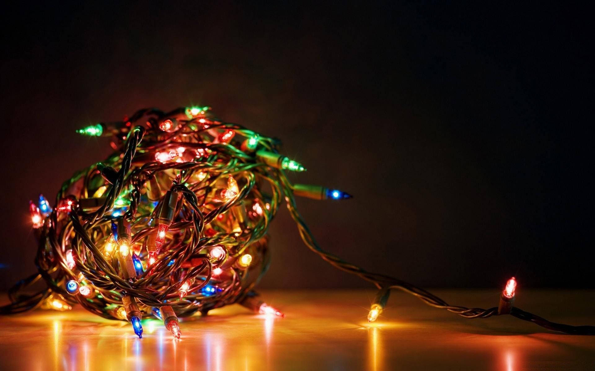 lights 桌布 壁紙 — 一束纏繞的彩色串燈在黑暗背景下的反射表面上溫暖地發光。