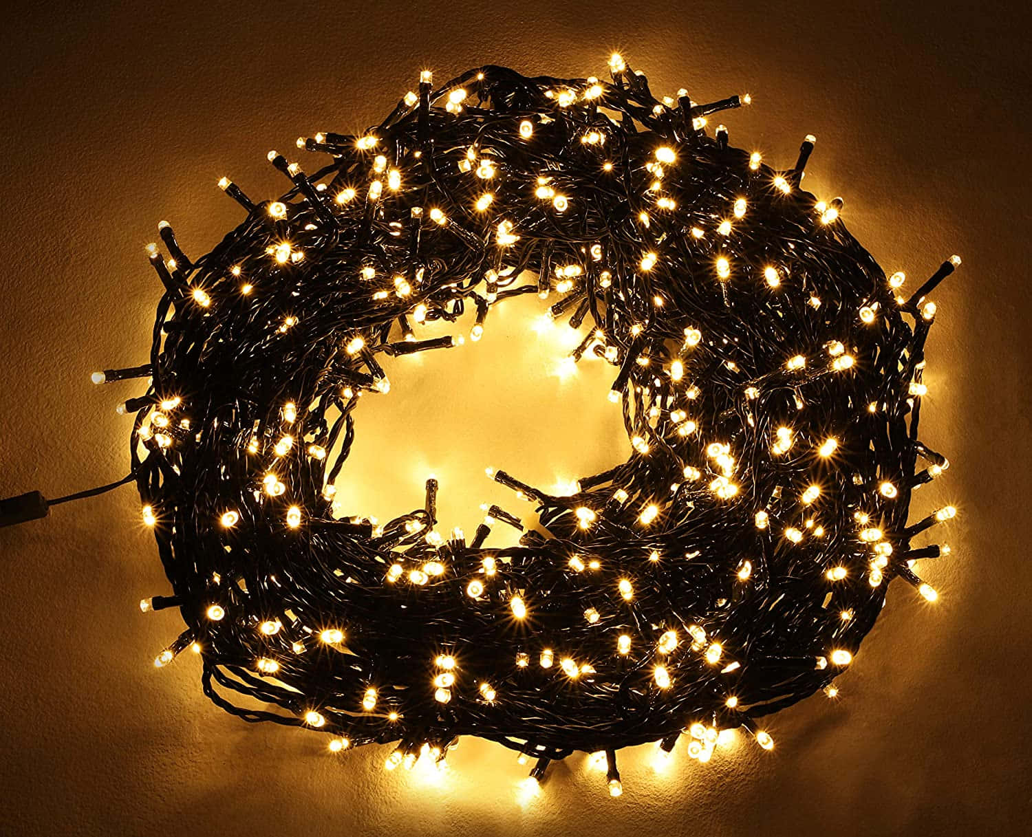 Led Light 桌布 壁紙 — 一束纏繞的暖白色仙女燈花環，在紋理牆壁上投射出柔和的金色光芒。