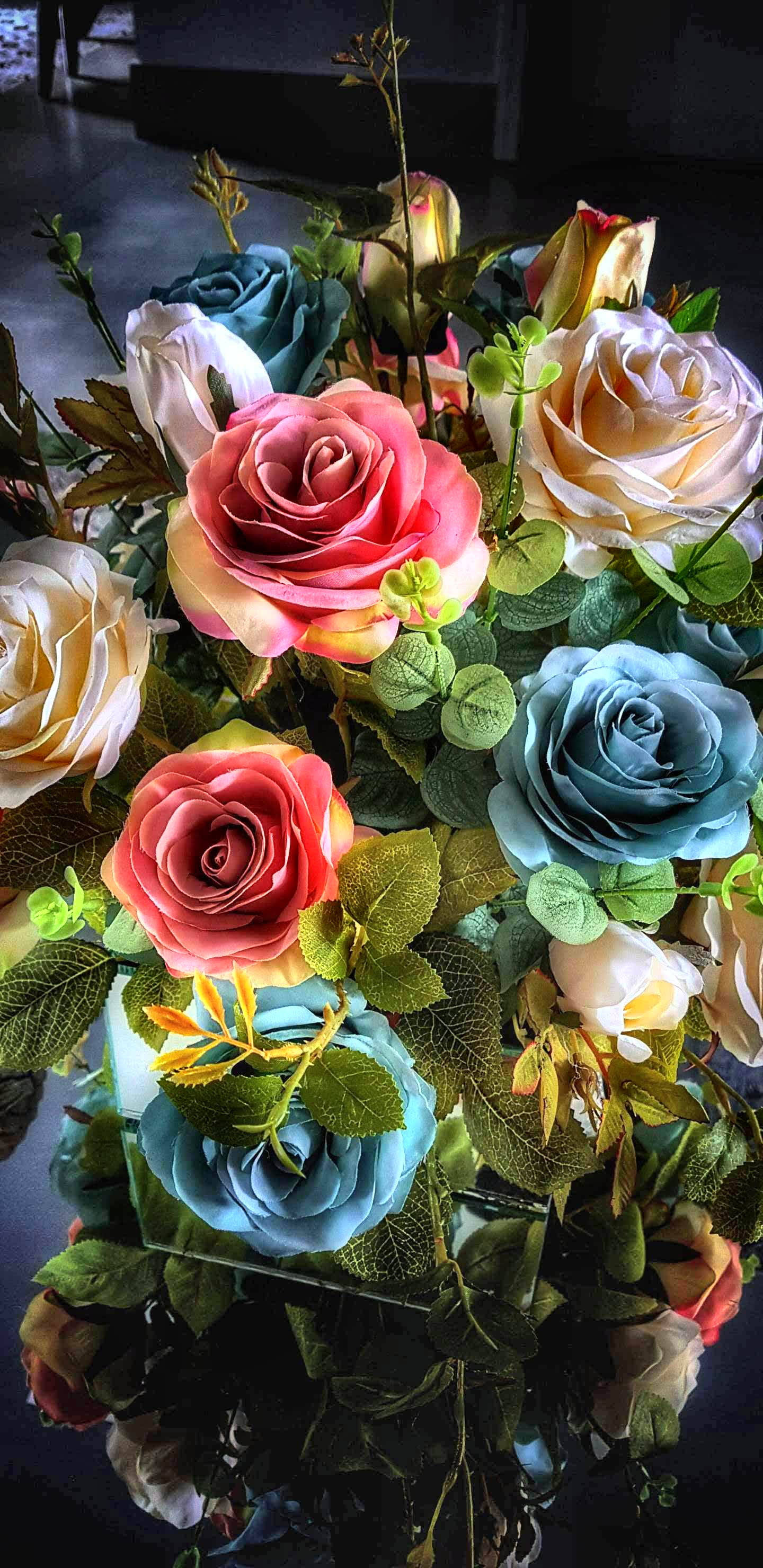 Roses 桌布 壁紙 — 一束色彩繽紛的玫瑰，包括粉紅、藍色和奶油色調，在戲劇性燈光下搭配茂盛的綠葉。