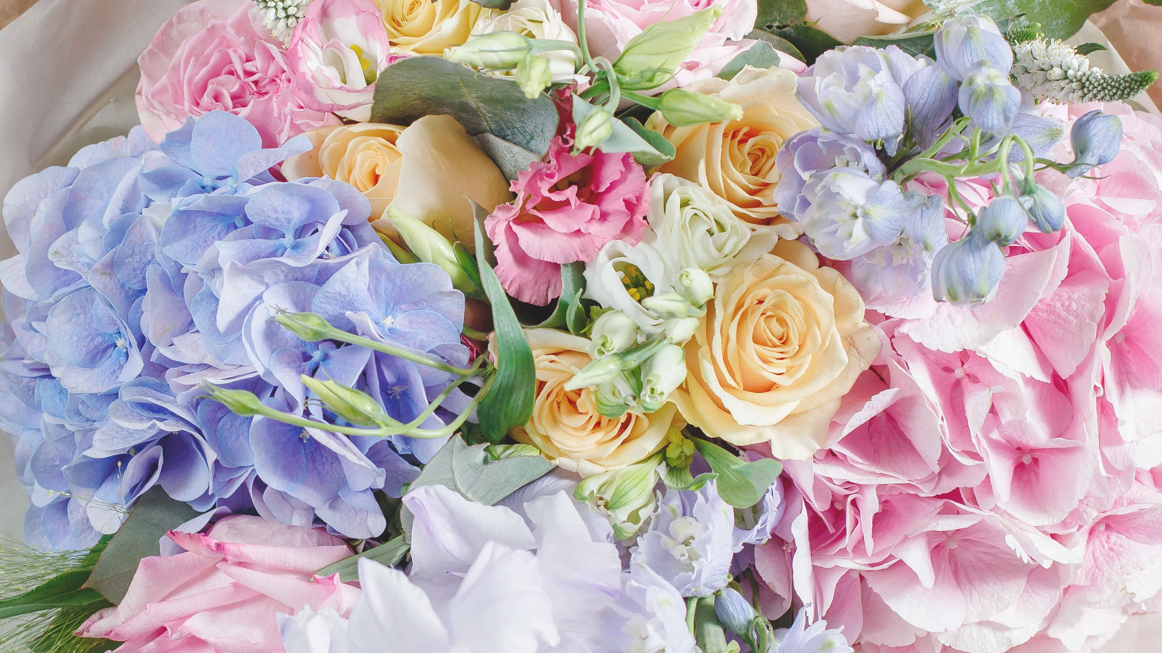 Colorful Flowers 桌布 壁紙 — 一束豐富的粉彩粉紅、藍色和黃色花朵，搭配綠葉，在柔和自然光線下擺放。