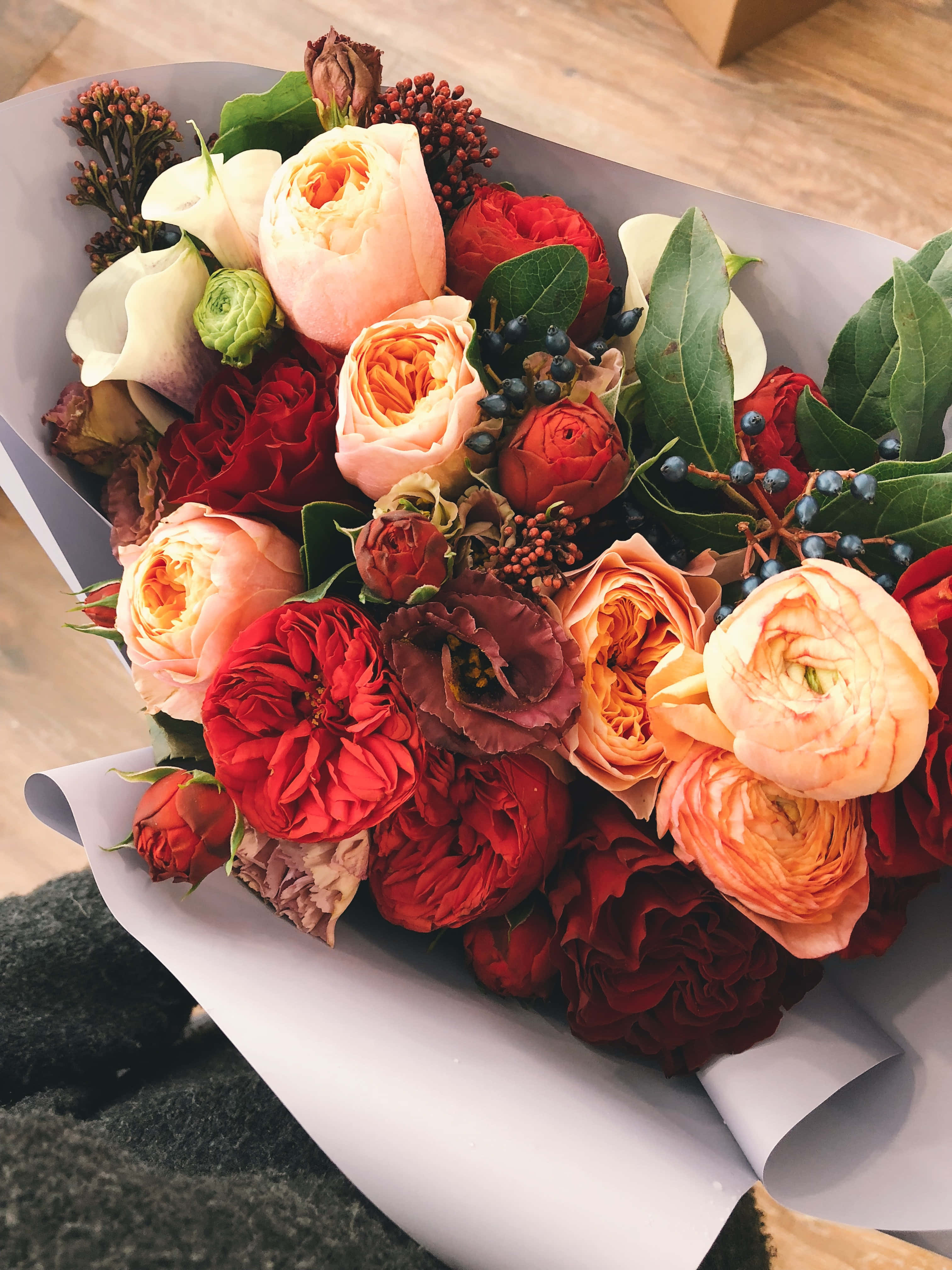 Bouquet 桌布 壁紙 — 一束豐盛的紅桃色和奶油色玫瑰，配以綠葉和漿果，用白紙包裹，放在木質表面上。