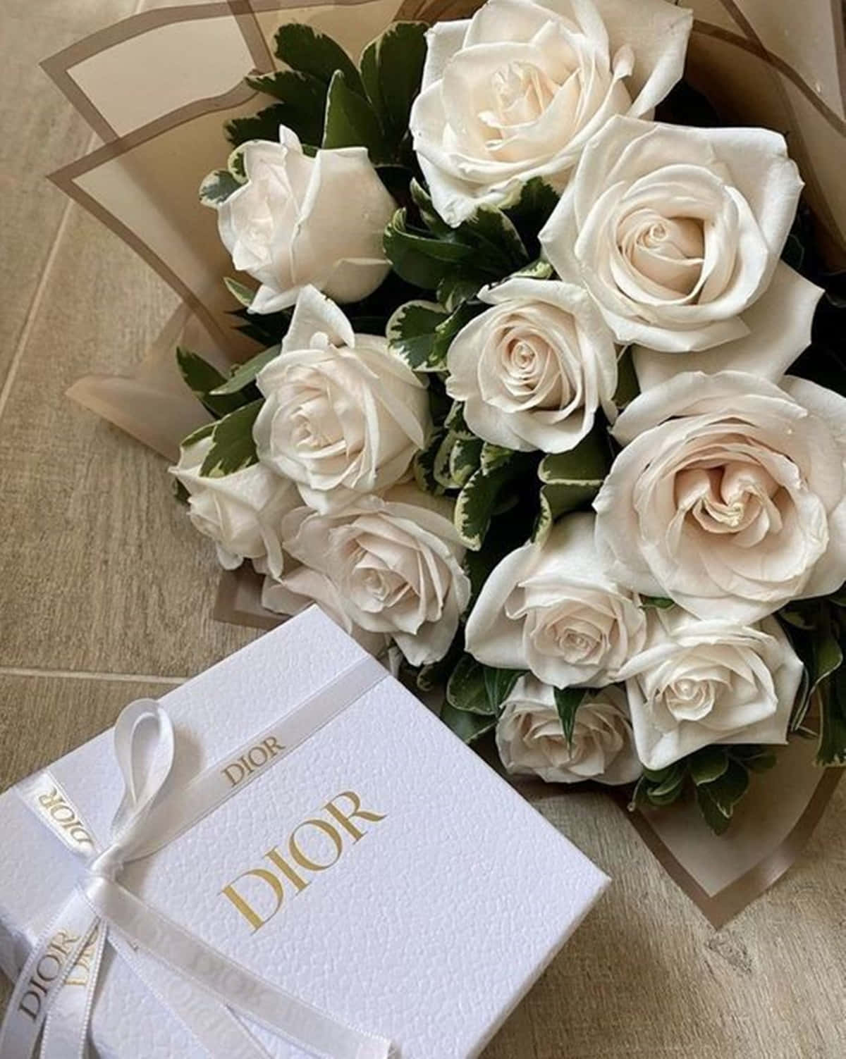 Roses 桌布 壁紙 — 一束豪華的奶油白玫瑰，搭配雜色綠葉，放在淺色木地板上，旁邊是一個繫著白色絲帶的Dior禮物盒。