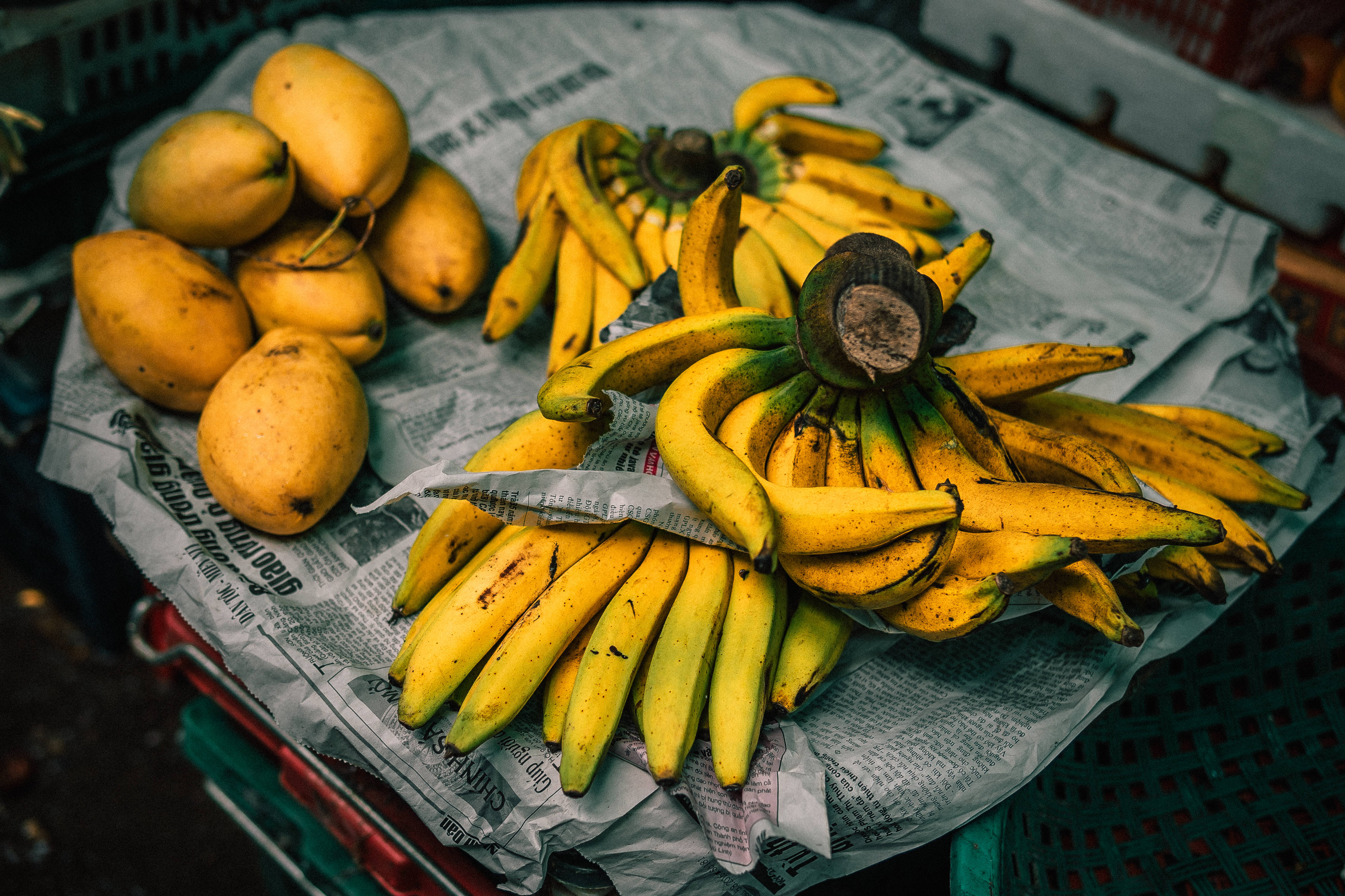 Fruits 桌布 壁紙 — 一束鮮豔的成熟香蕉和黃芒果放在市場攤位的皺報紙上。