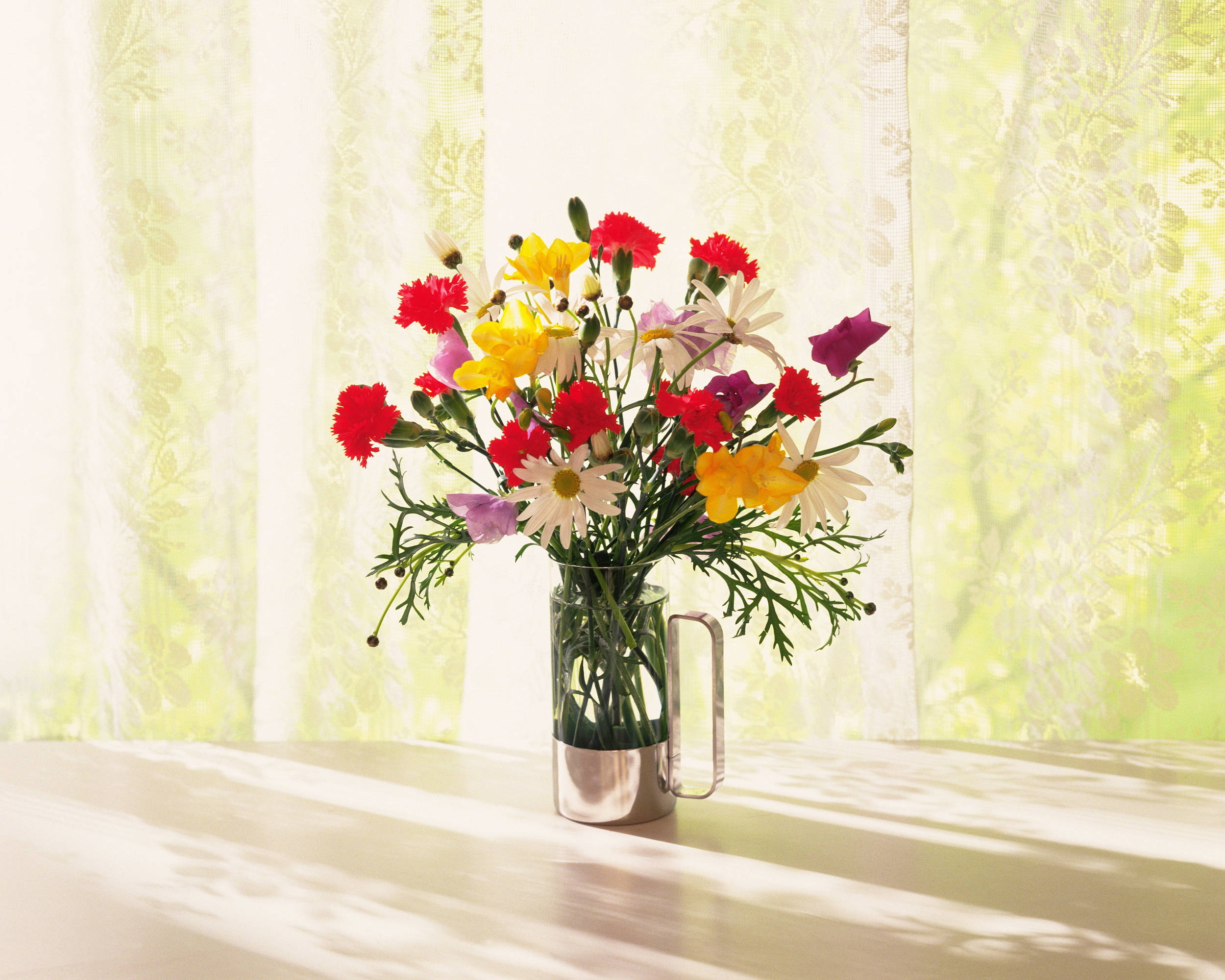 Bouquet 桌布 壁紙 — 一束鮮豔的紅、黃、紫色花朵插在玻璃花瓶中，放在陽光灑落的窗台上，薄紗窗簾投下柔和的陰影。