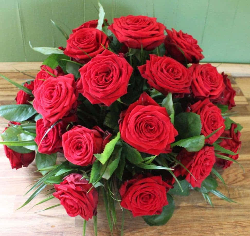Rose Flower 桌布 壁紙 — 一束鮮豔的紅玫瑰和綠葉放在木質表面上，背景是綠色牆壁。