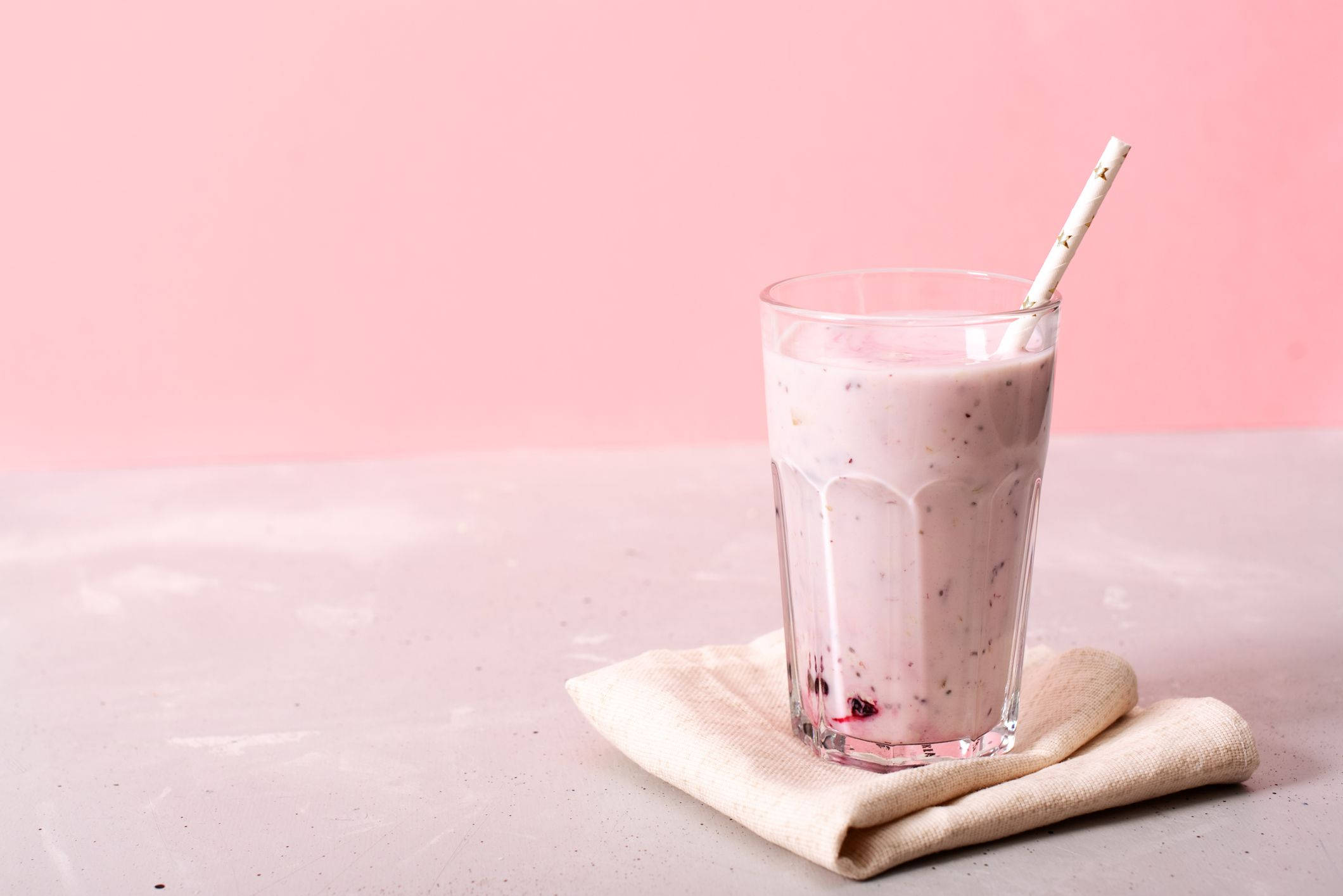Smoothie 桌布 壁紙 — 一杯 creamy 粉紅莓果 smoothie，盛載於紋理玻璃杯中，附有吸管，置於米色餐巾上，襯以柔和粉紅背景。