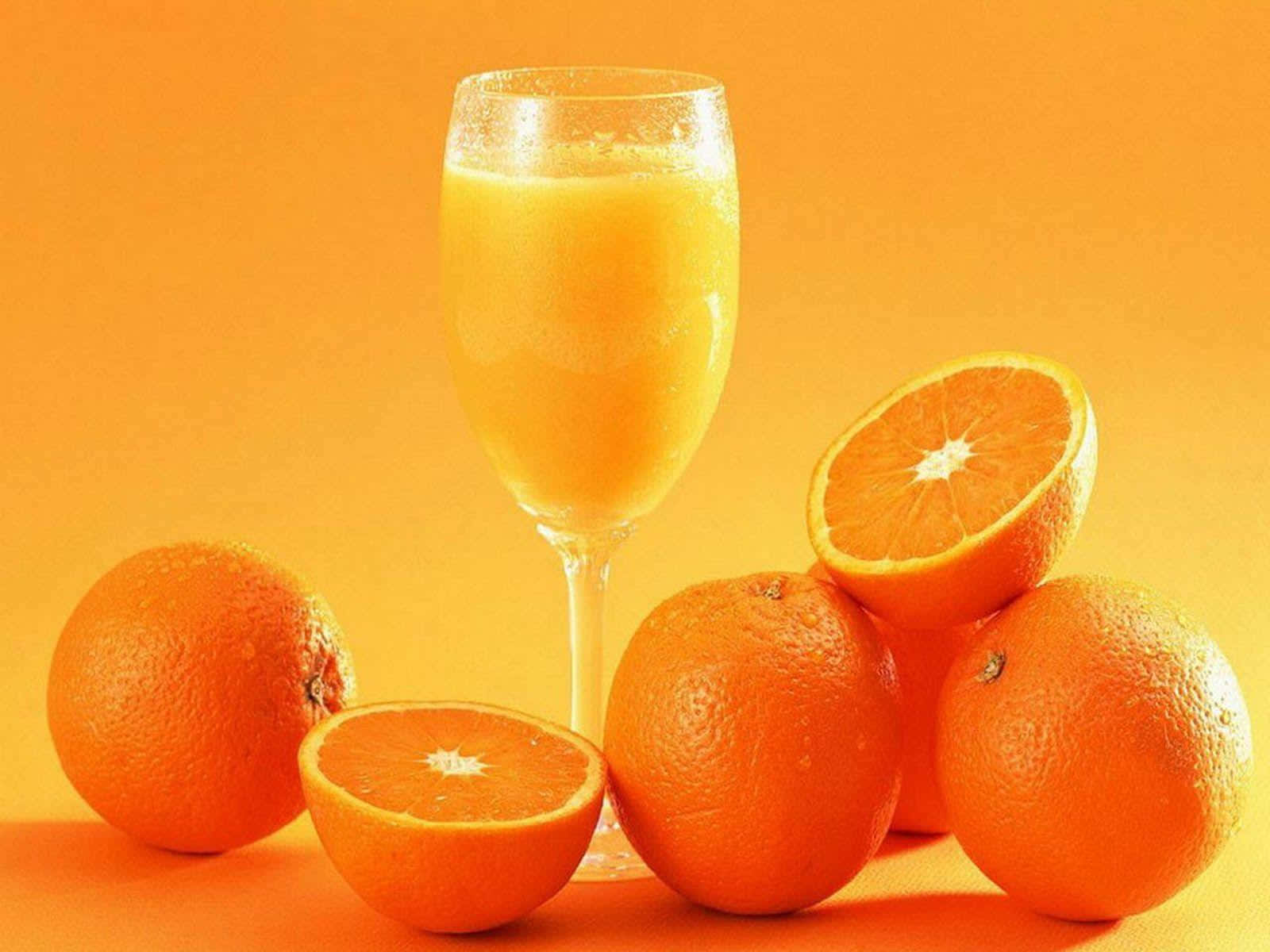 Orange Fruit 桌布 壁紙 — 一杯充滿活力的柳橙汁，周圍環繞著完整和半切的柳橙，背景是溫暖的橙色。