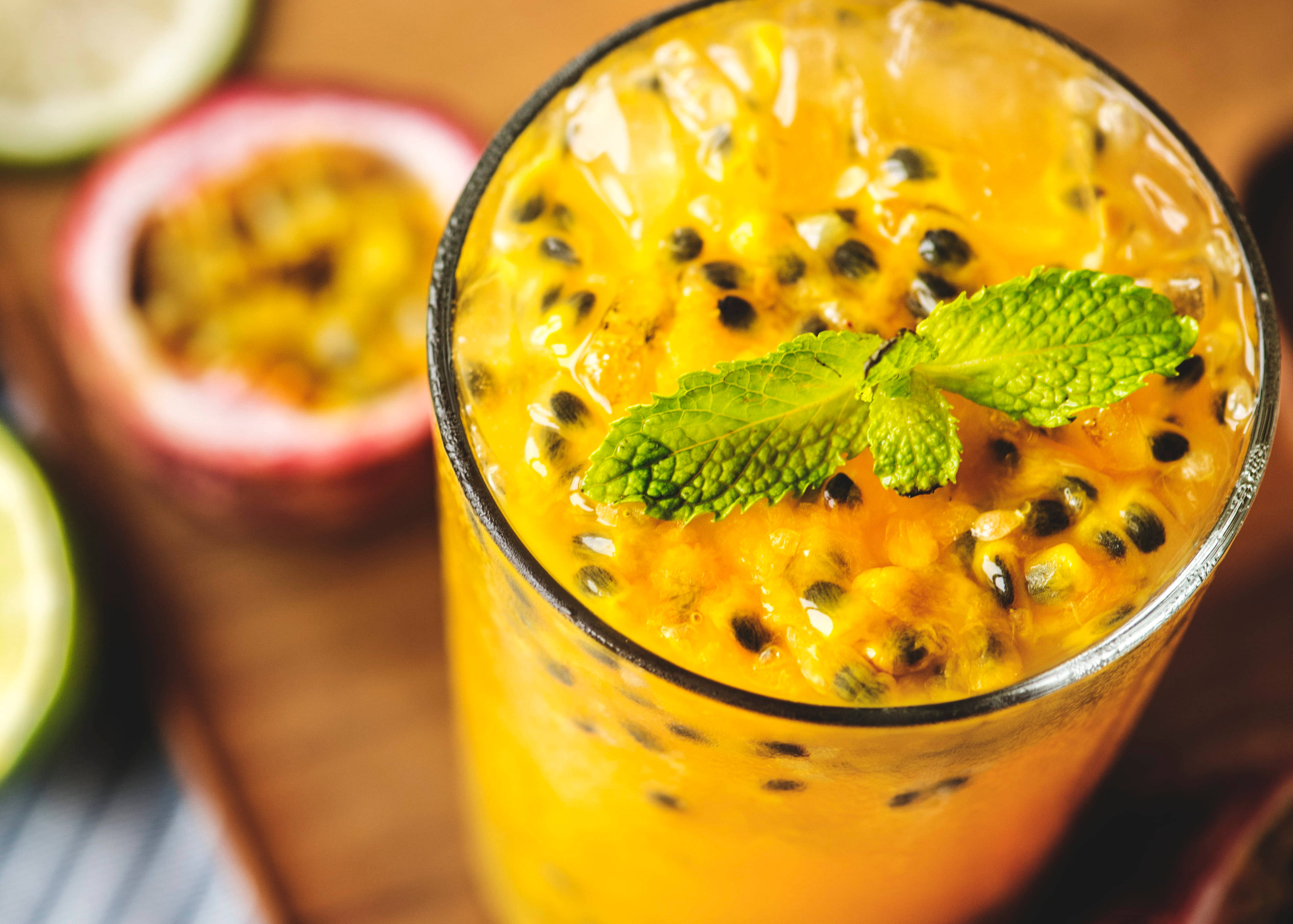 Fruits 桌布 壁紙 — 一杯充滿活力的橙色百香果飲品，上面放有薄荷和冰塊，旁邊有切半的百香果和萊姆，置於木質表面上。