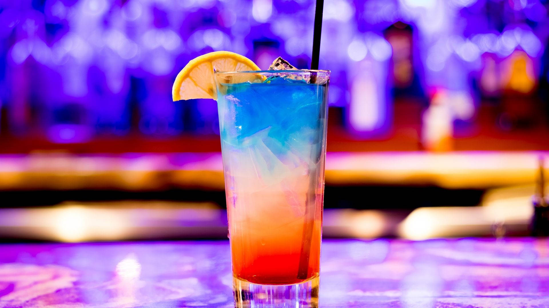Drink 桌布 壁紙 — 一杯充滿活力的漸層雞尾酒，配上檸檬裝飾，放在紫色霓虹燈下的酒吧上。