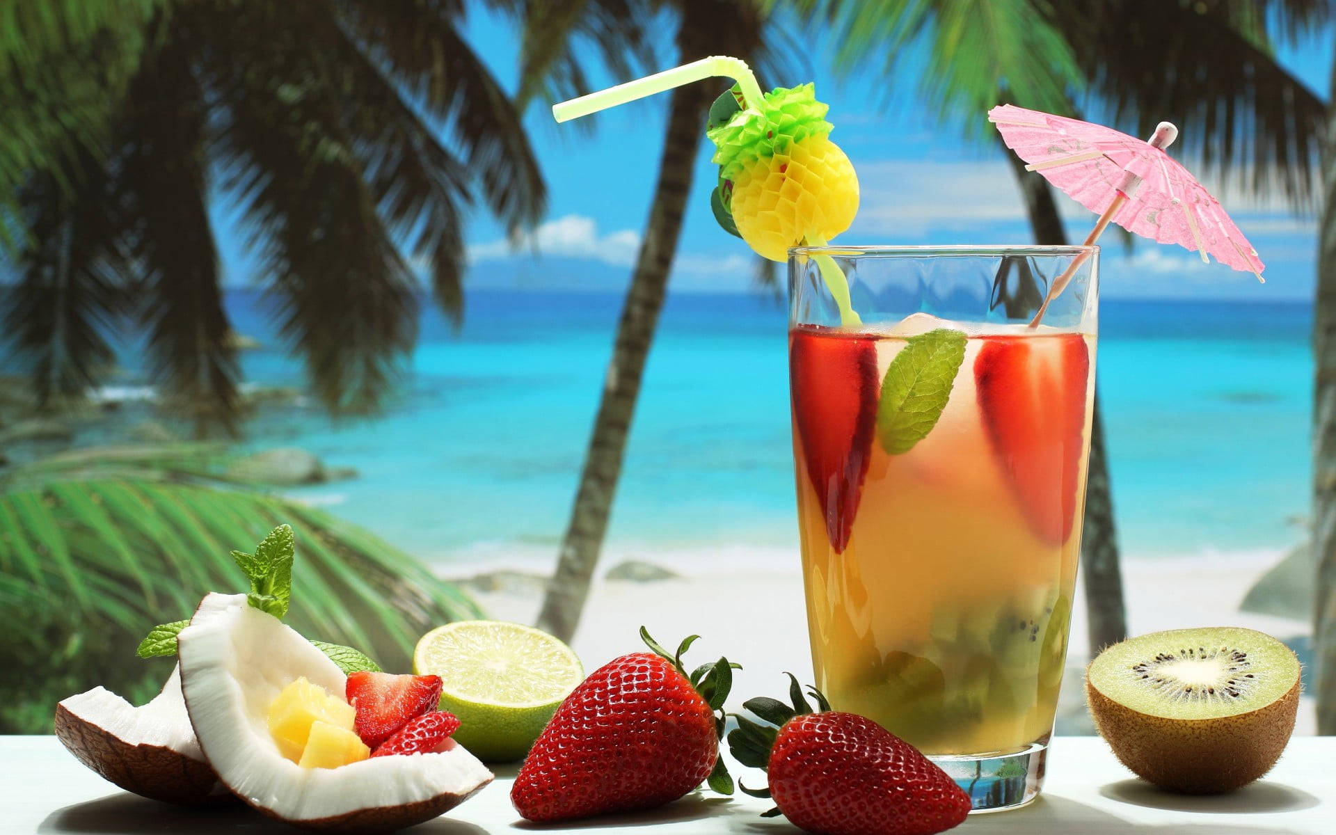 Tropical Drink 桌布 壁紙 — 一杯充滿活力的熱帶雞尾酒，配上新鮮水果裝飾，放在桌子上，背景是棕櫚樹和碧綠的海洋。