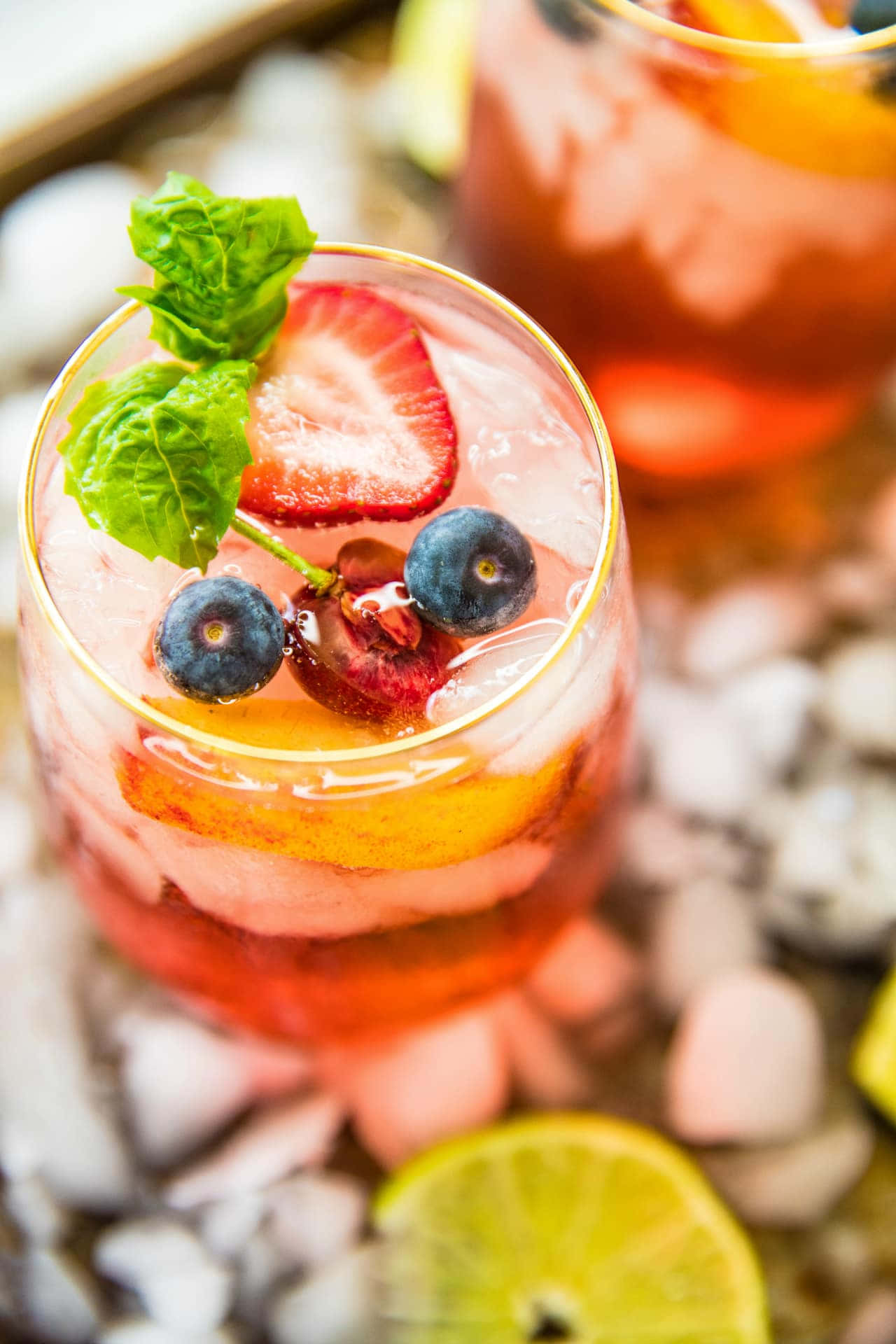 Beautiful Drink 桌布 壁紙 — 一杯充滿活力的粉紅色雞尾酒，盛載於金邊玻璃杯中，上面放有新鮮莓果、薄荷和冰塊，置於碎冰床上。
