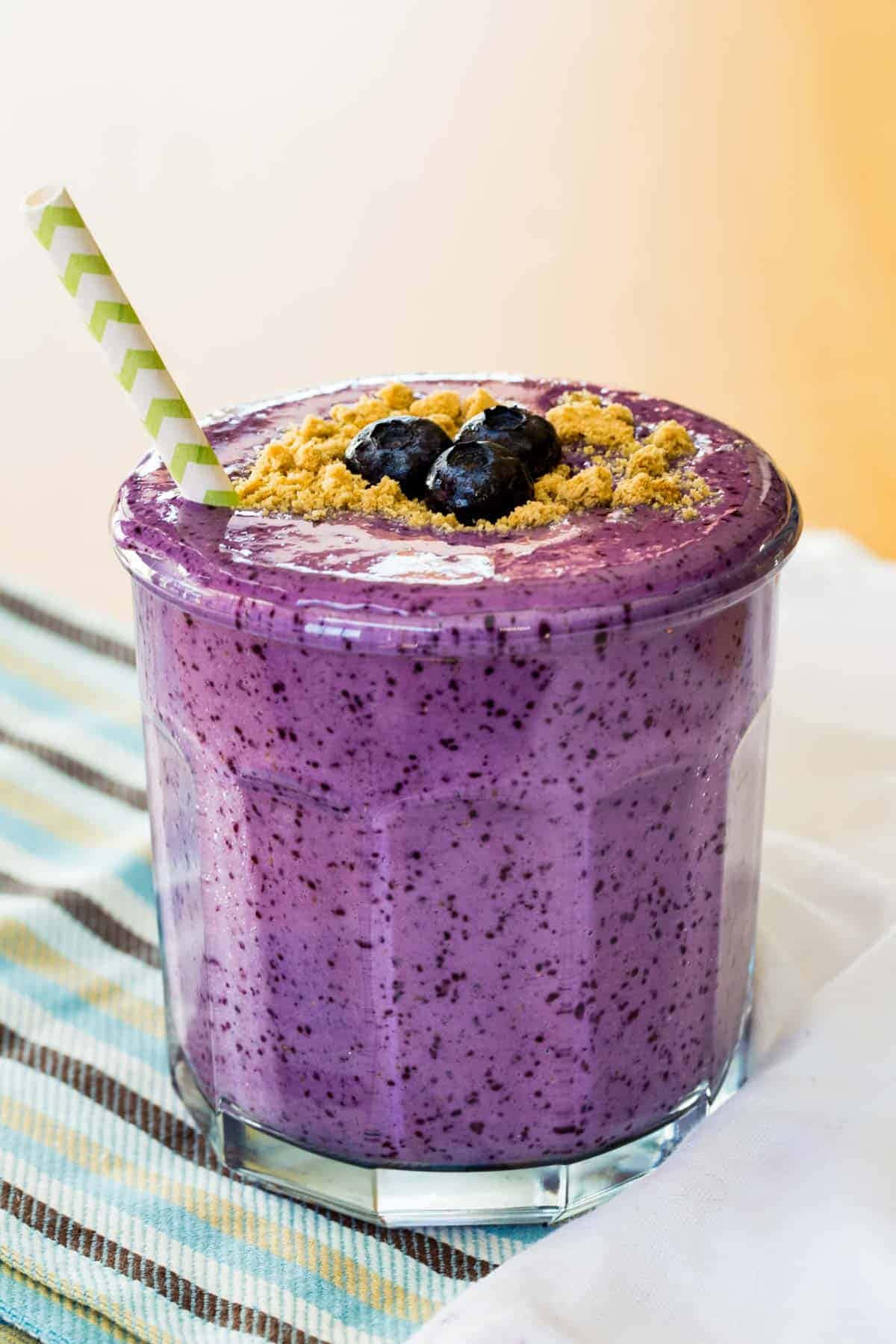 Blueberry Smoothie 桌布 壁紙 — 一杯充滿活力的紫色藍莓冰沙，上面放有藍莓和壓碎的格雷厄姆餅乾，配上一條條紋吸管。