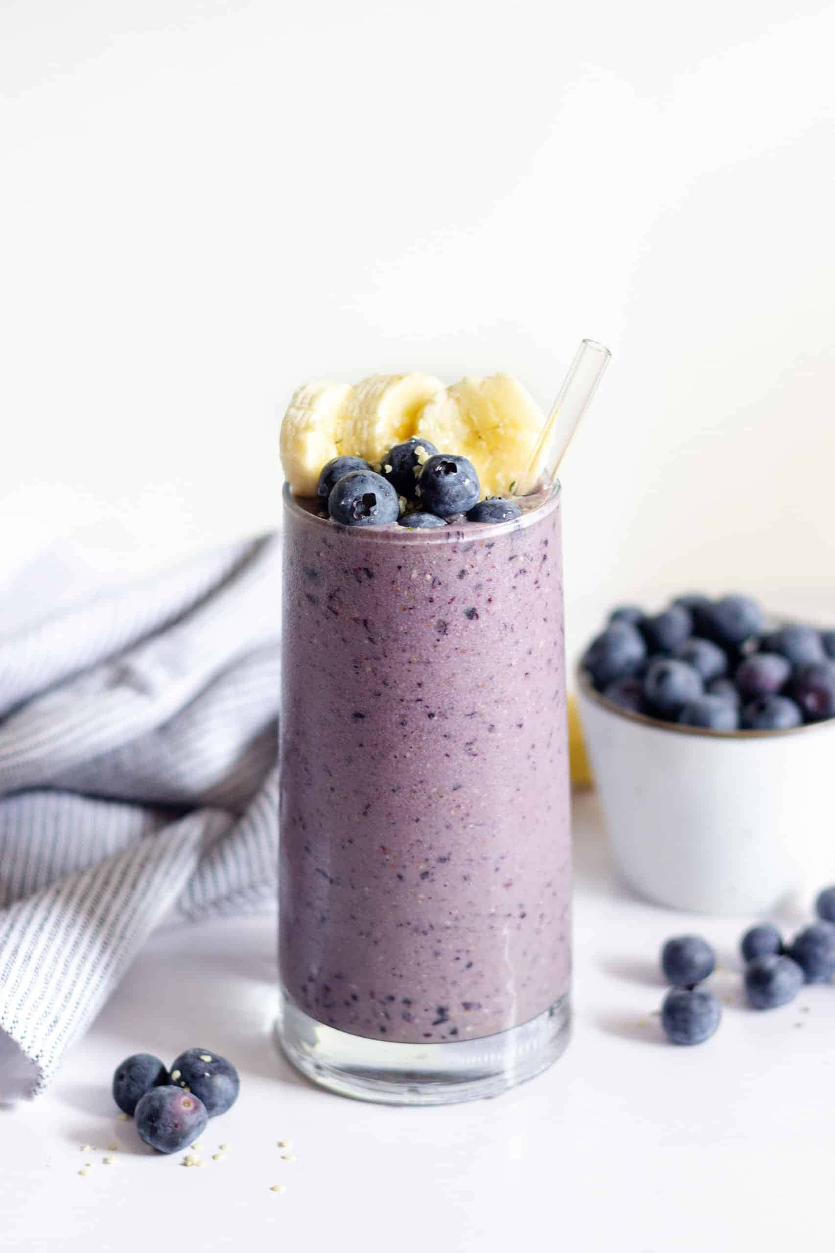 Blueberry Smoothie 桌布 壁紙 — 一杯充滿活力的紫藍莓香蕉奶昔，配上新鮮水果，盛載於透明玻璃杯中，以亮白色背景襯托。