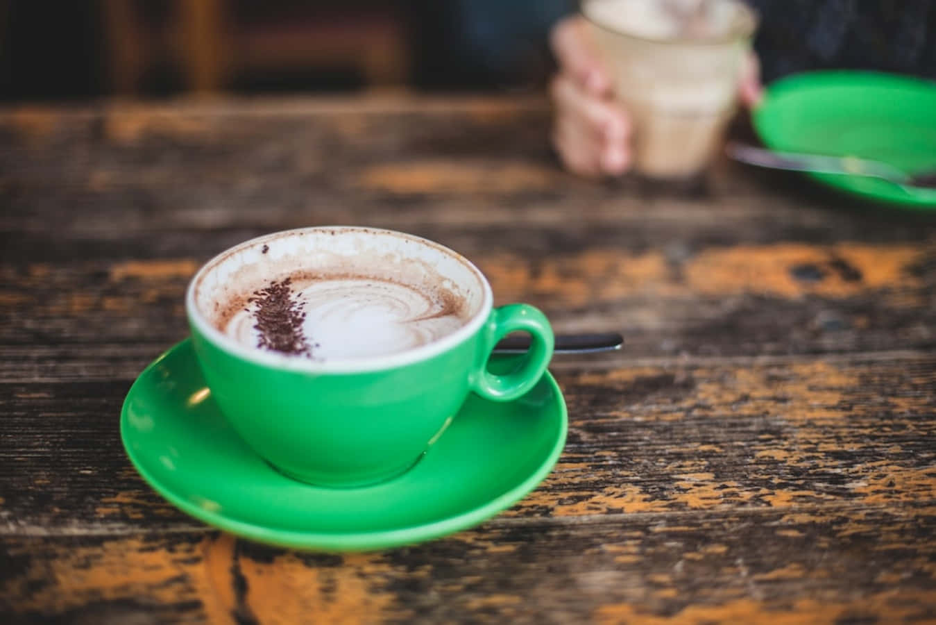 Morning Coffee 桌布 壁紙 — 一杯充滿活力的綠色卡布奇諾，帶有可可粉漩渦，放在舒適咖啡館的質樸木桌上。