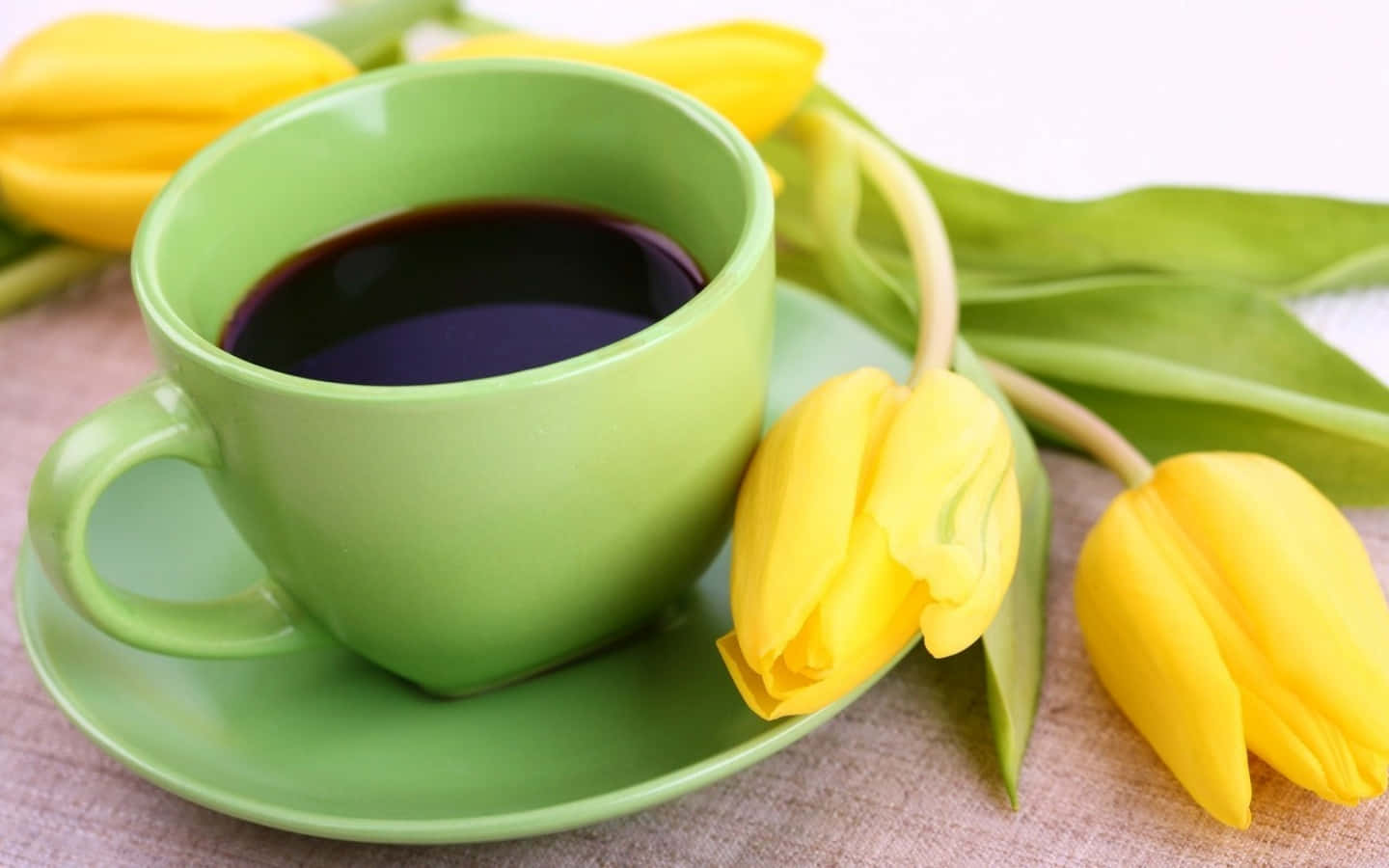 Morning Coffee 桌布 壁紙 — 一杯充滿活力的綠色深色咖啡放在碟子上，旁邊是質感表面上的新鮮黃色鬱金香。