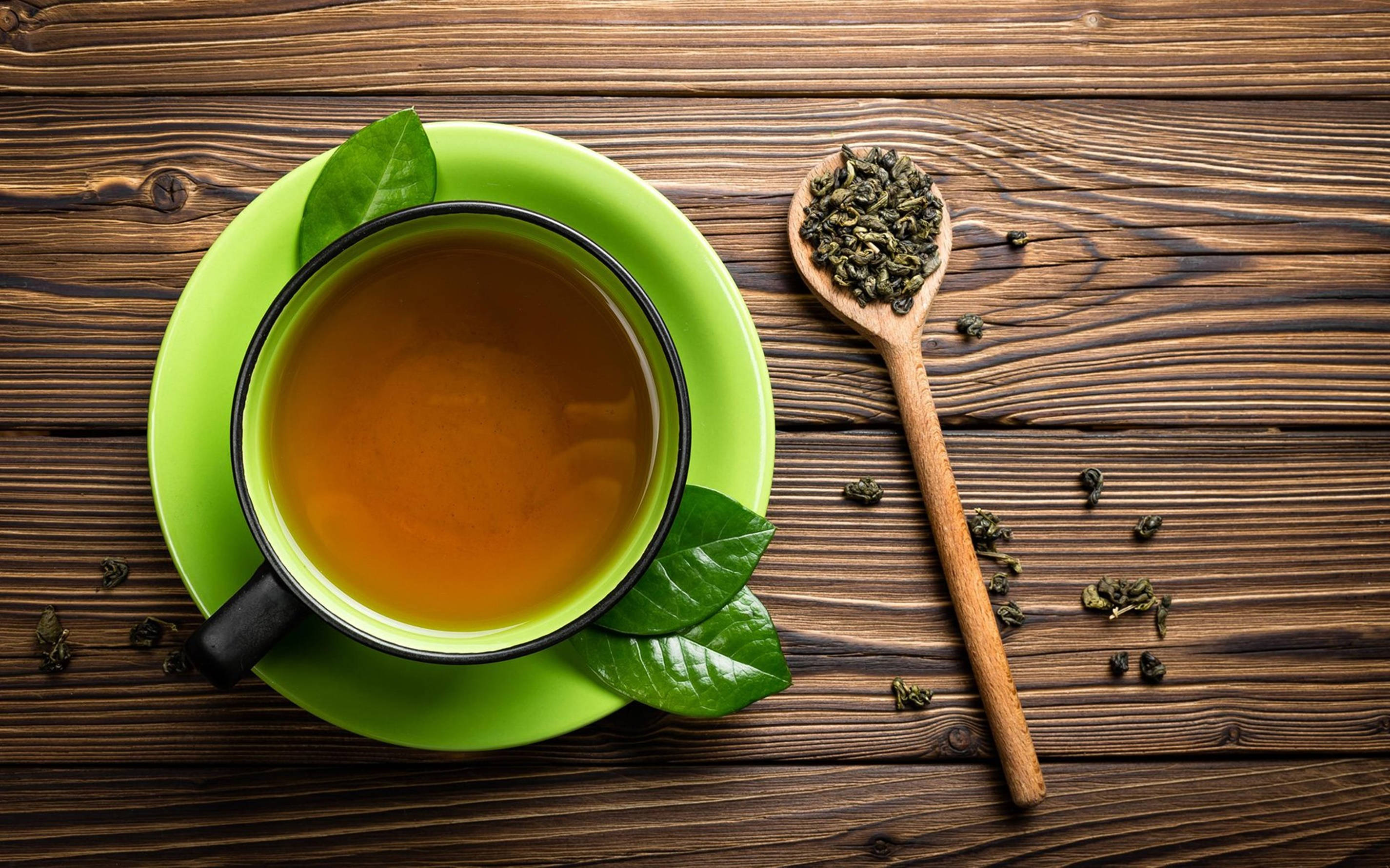 tea 桌布 壁紙 — 一杯充滿活力的綠色熱茶放在質樸的木桌上，旁邊的木匙裝滿了鬆散的綠茶葉。