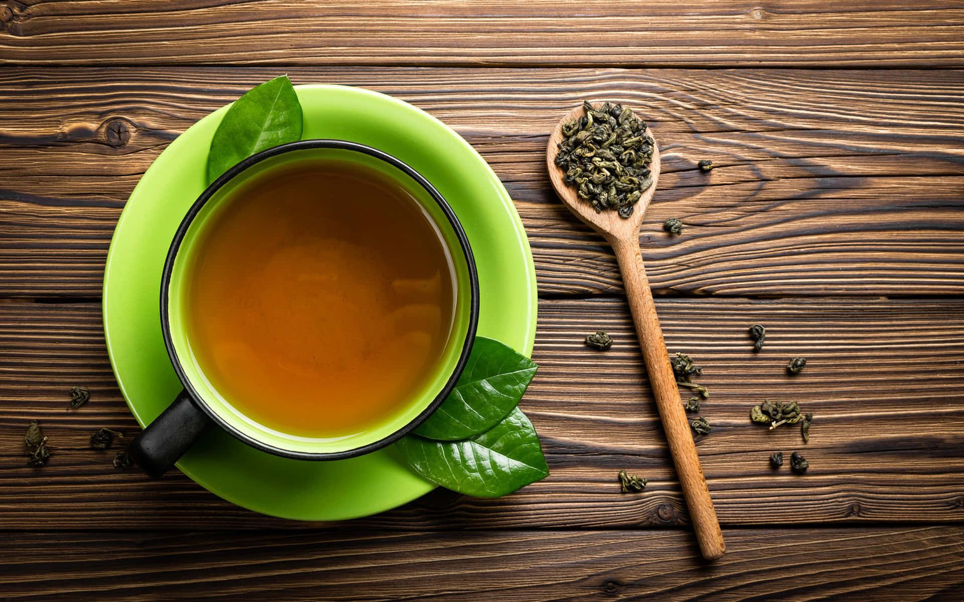 tea 桌布 壁紙 — 一杯充滿活力的綠茶放在質樸的木桌上，旁邊的木匙盛著散裝茶葉和新鮮綠葉。