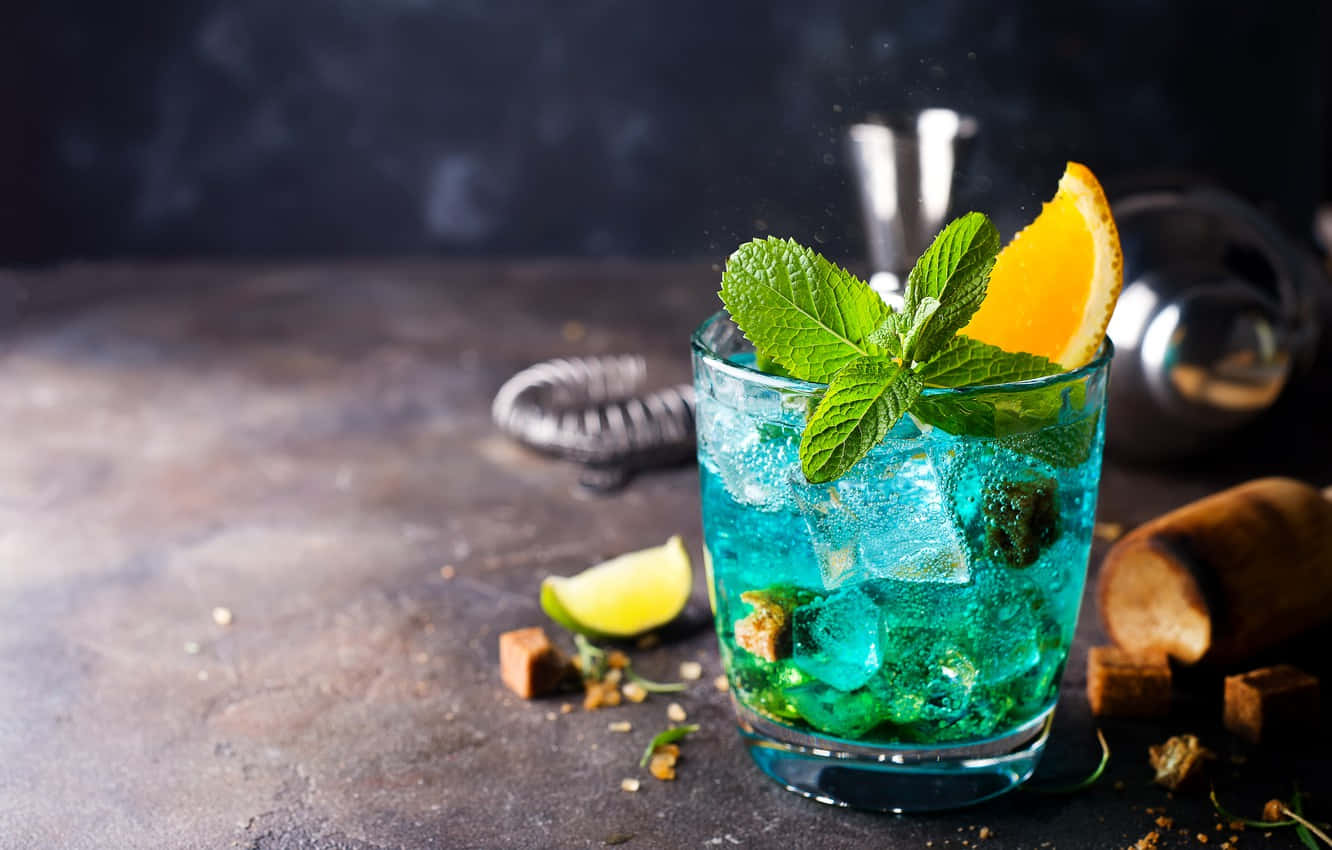 alcohol 桌布 壁紙 — 一杯充滿活力的藍色雞尾酒，配上薄荷和橙裝飾，放在深色紋理表面上，周圍有酒吧工具和方糖。