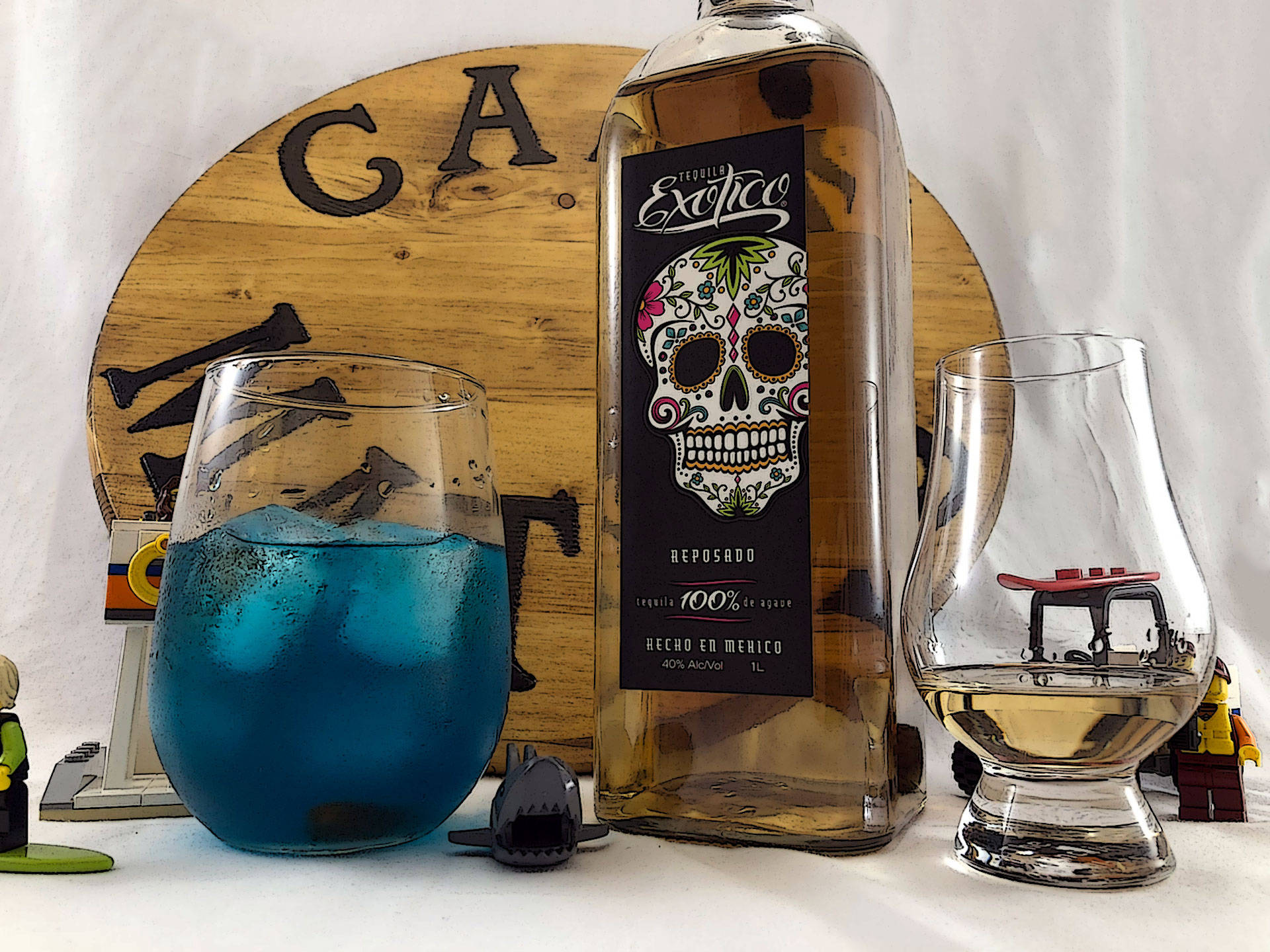 cocktail 桌布 壁紙 — 一杯充滿活力的藍色雞尾酒加冰，旁邊放著一瓶帶有彩色糖骷髏標籤的龍舌蘭酒和一杯琥珀色液體，周圍有LEGO人偶在白色表面上。