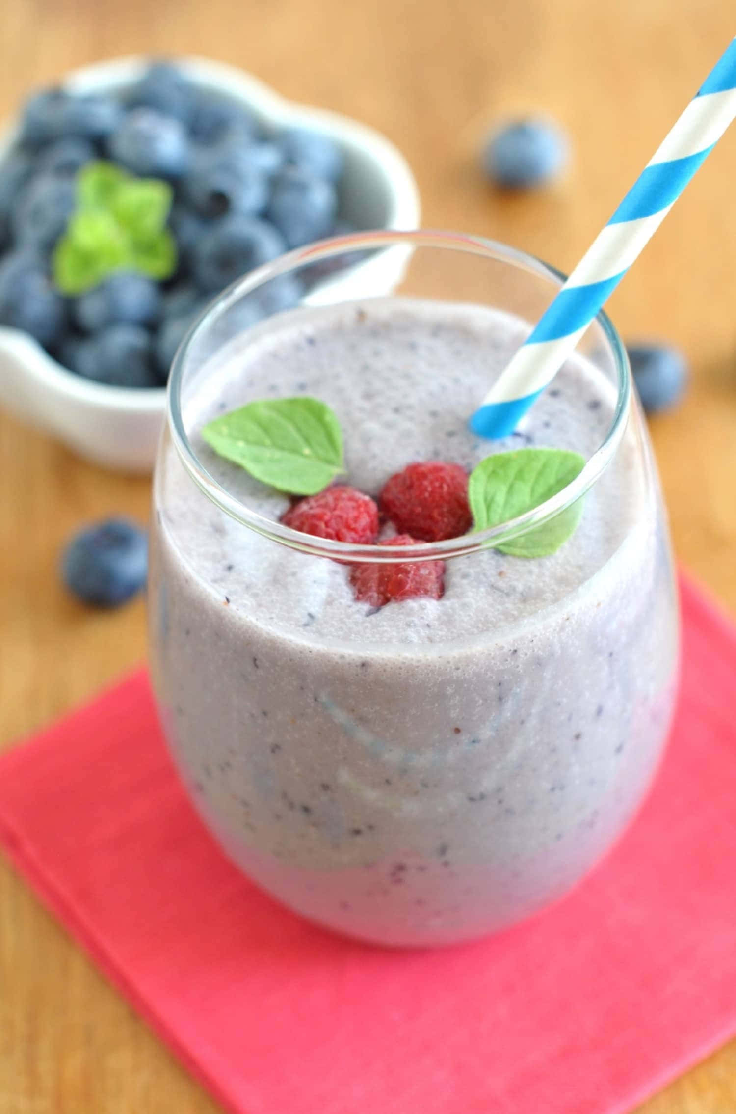 Blueberry Smoothie 桌布 壁紙 — 一杯充滿活力的藍莓覆盆子冰沙，上面放著新鮮莓果和薄荷，放在粉紅色餐巾上。