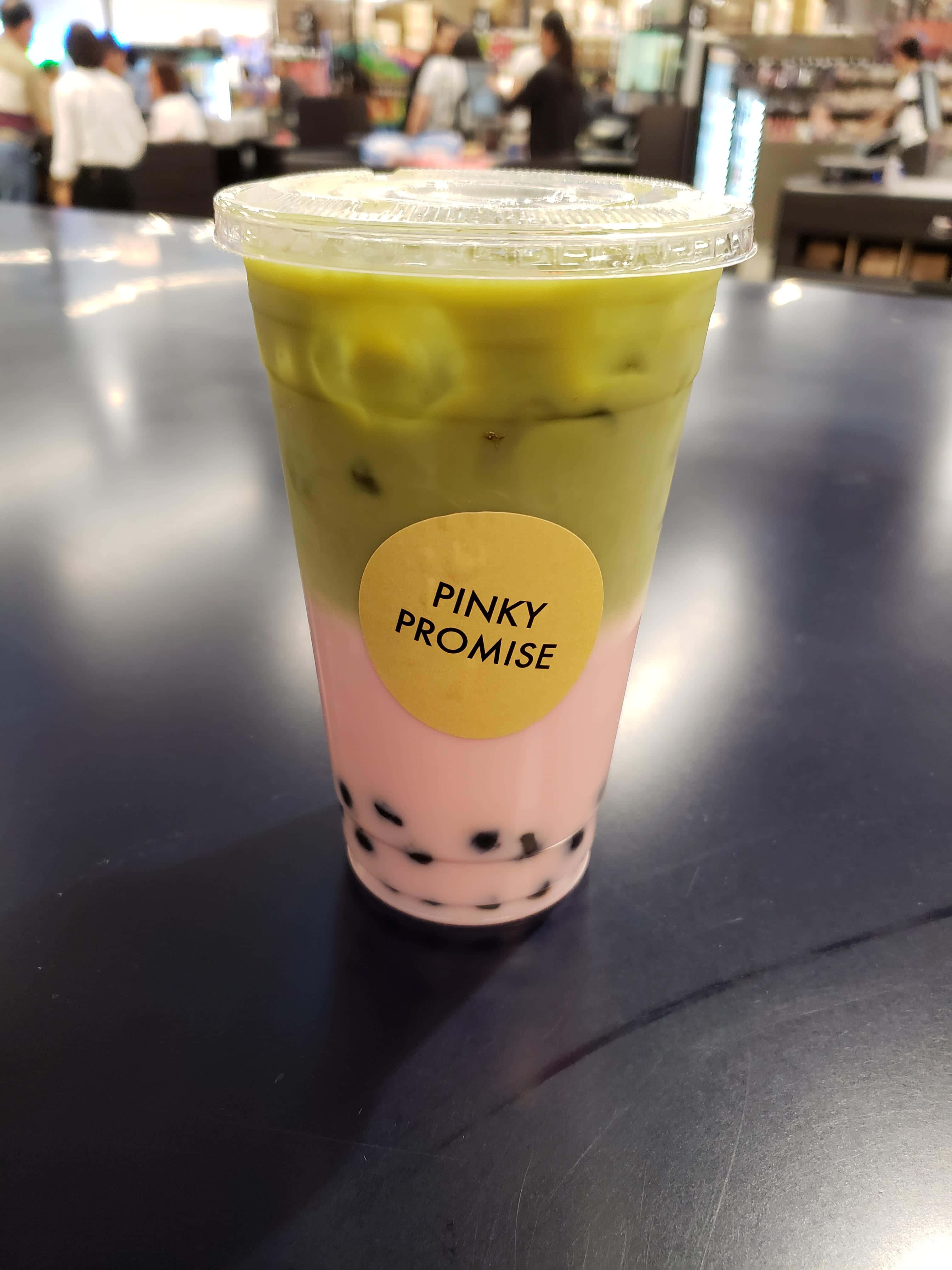 Boba Tea 桌布 壁紙 — 一杯充滿活力的雙色泡泡茶，粉紅奶底和綠茶層，加上冰塊，放在繁忙咖啡館的深色桌子上。
