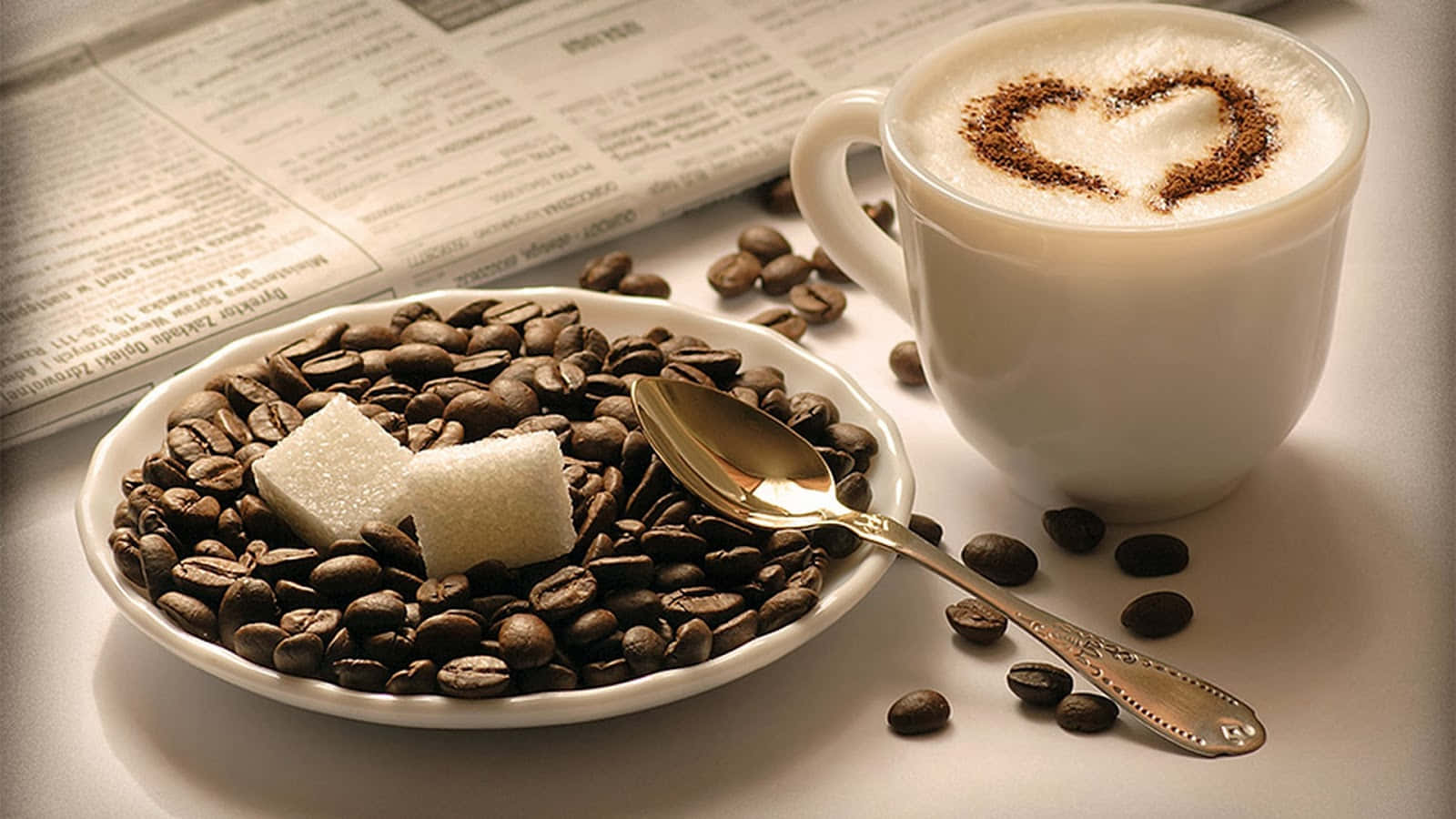 Coffee Cup 桌布 壁紙 — 一杯冒煙的卡布奇諾，上面有心形可可粉，旁邊放著一碟咖啡豆和方糖在報紙上。