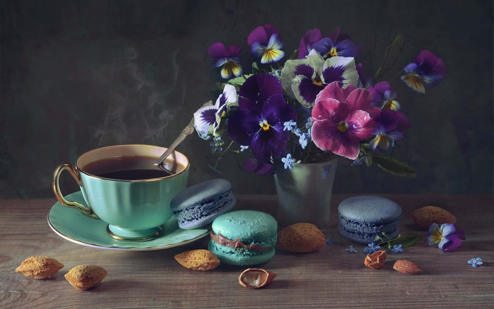 Spring Desserts 桌布 壁紙 — 一杯冒煙的咖啡，旁邊是鮮豔的紫色和粉紅色三色堇，以及色彩繽紛的馬卡龍，放在質樸的木桌上。