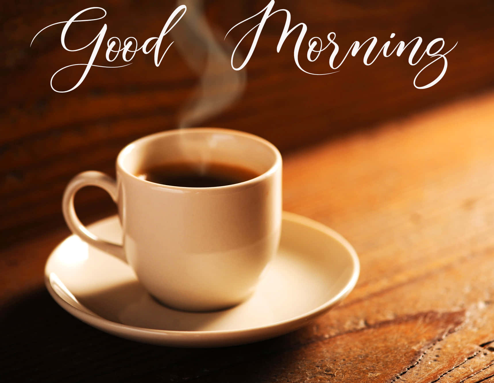 Morning Coffee 桌布 壁紙 — 一杯冒煙的咖啡放在木桌上，上方以優雅的白色草書寫著「早安」。