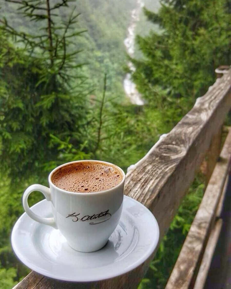 Morning Coffee 桌布 壁紙 — 一杯冒煙的咖啡放在木欄杆上，俯瞰下方鬱鬱蔥蔥的森林和蜿蜒的河流。