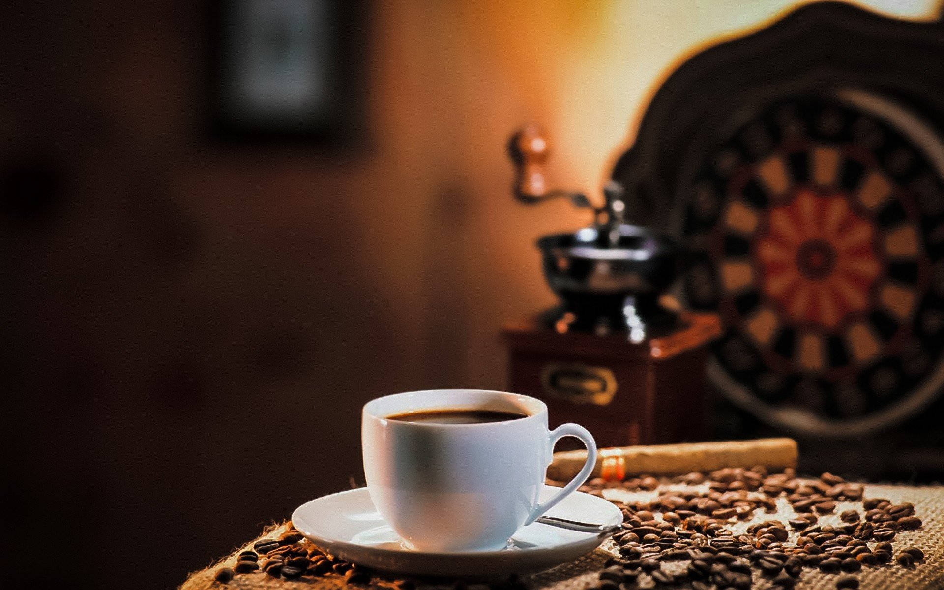 Coffee Aesthetic 桌布 壁紙 — 一杯冒煙的咖啡放在碟子上，周圍有咖啡豆，背景是溫暖模糊的復古研磨機和飛鏢靶。