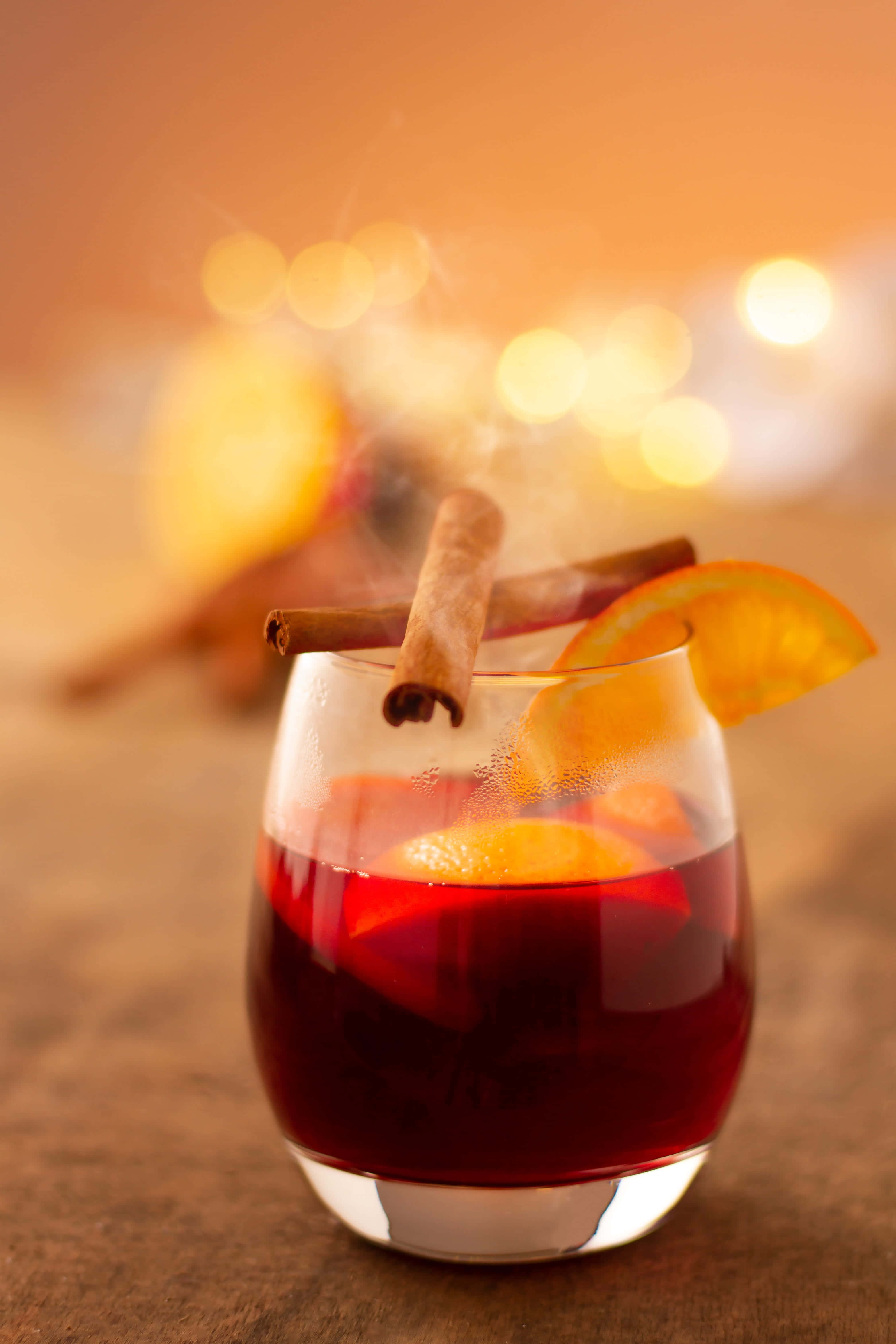 Mulled Wine 桌布 壁紙 — 一杯冒煙的熱紅酒，飾以橙片和肉桂棒，在散景燈光背景下溫暖地發光。