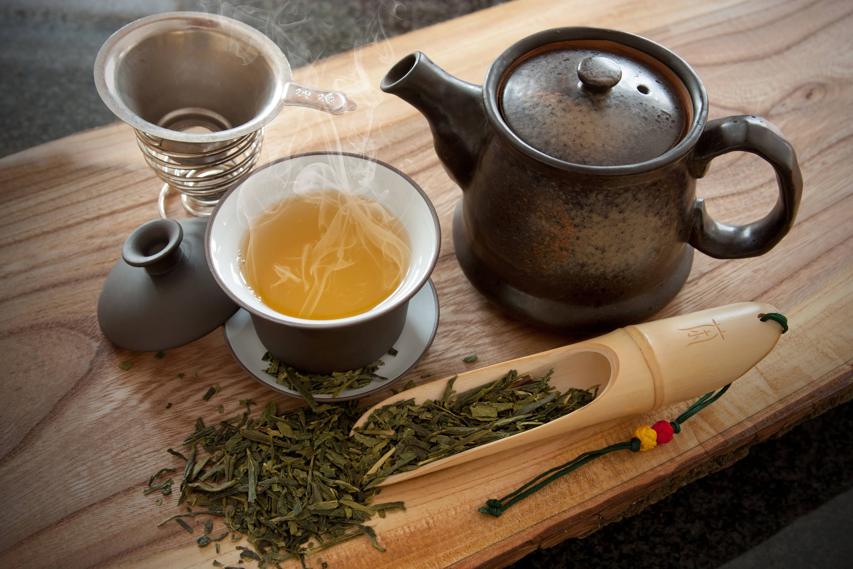 tea bag 桌布 壁紙 — 一杯冒煙的綠茶旁邊放著陶瓷茶壺和竹茶匙，置於鄉村風木桌上。