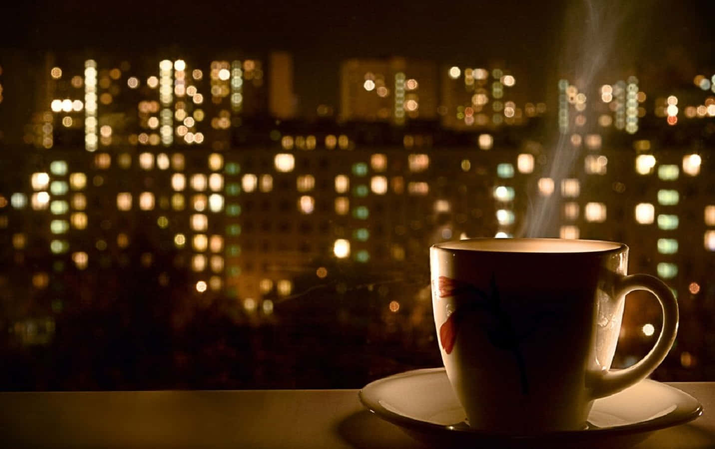 tea 桌布 壁紙 — 一杯冒煙的茶放在窗台上，俯瞰著柔和模糊的城市景觀，溫暖的夜燈閃爍著光芒。