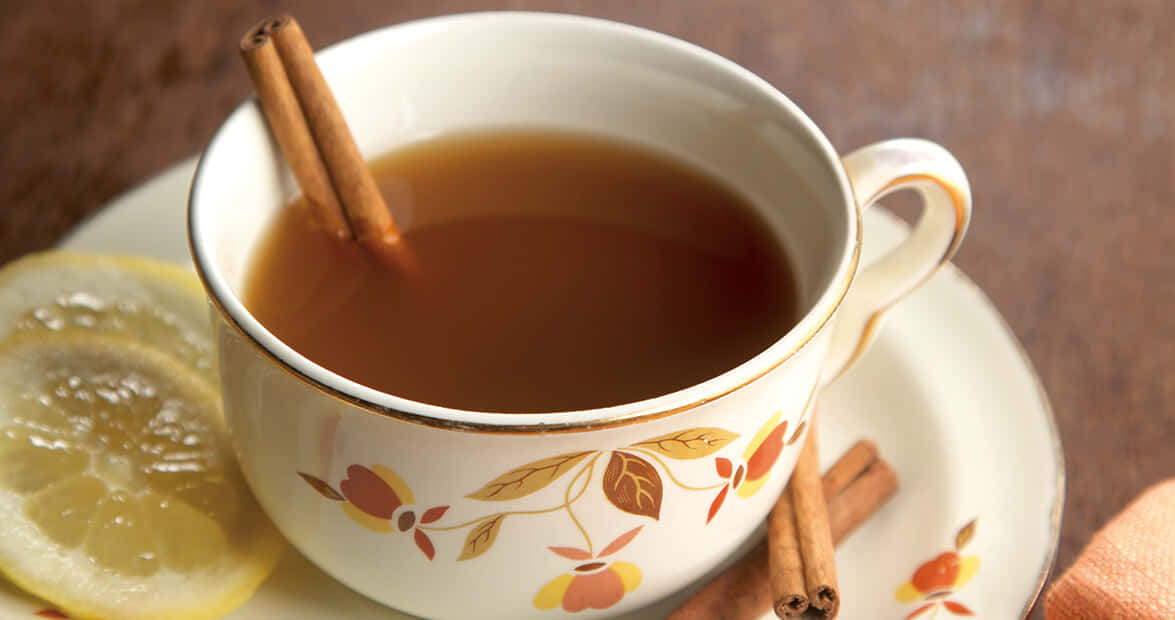 Morning Tea 桌布 壁紙 — 一杯冒煙的香料茶，搭配肉桂棒和檸檬片，放在花卉圖案的碟子上。