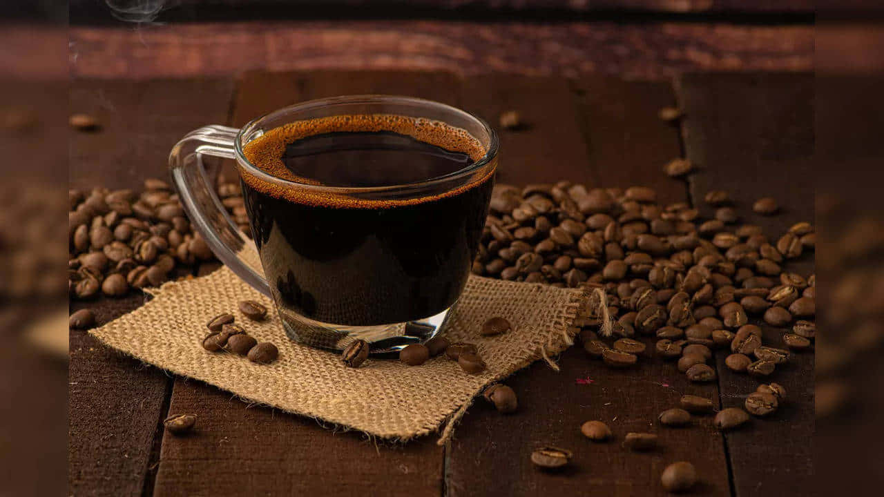 Brown Coffee 桌布 壁紙 — 一杯冒煙的黑咖啡放在粗麻布上，周圍是烘焙過的咖啡豆，置於鄉村風木桌上。