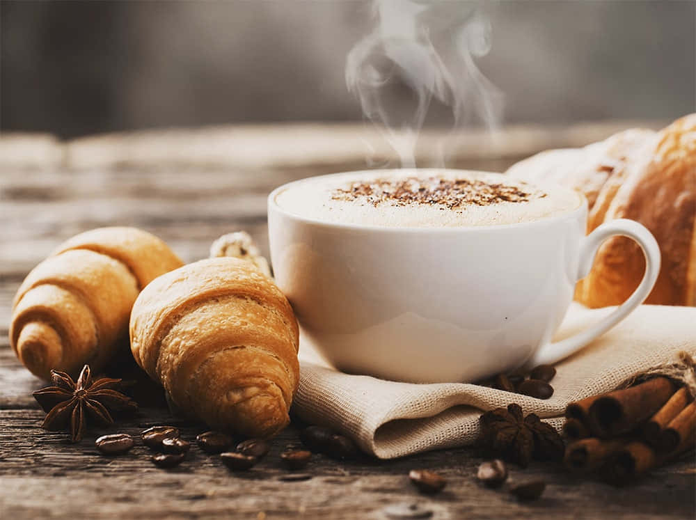 Milk And Coffee 桌布 壁紙 — 一杯冒著熱氣的咖啡，配上肉桂和八角，放在鄉村風木桌上，旁邊是金黃色的可頌。